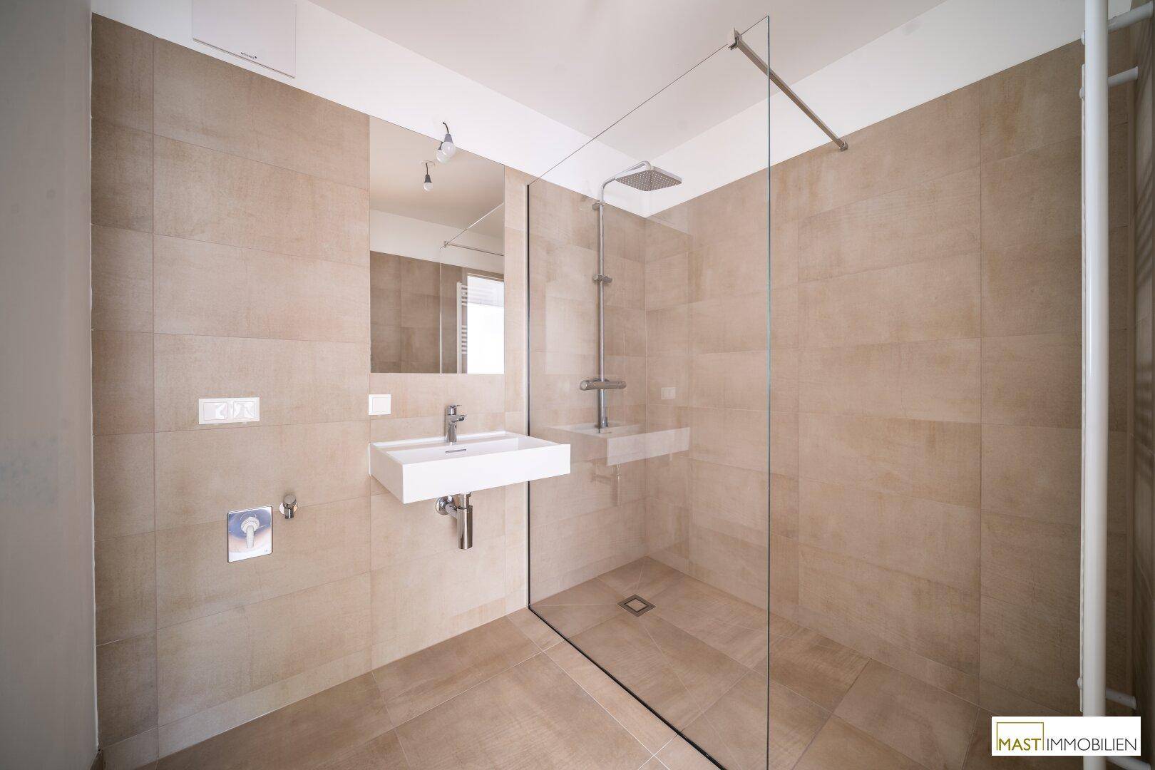 Elegantes Badezimmer mit beigefarbenen Fliesen, modernem Waschbecken und großer begehbarer Dusche.