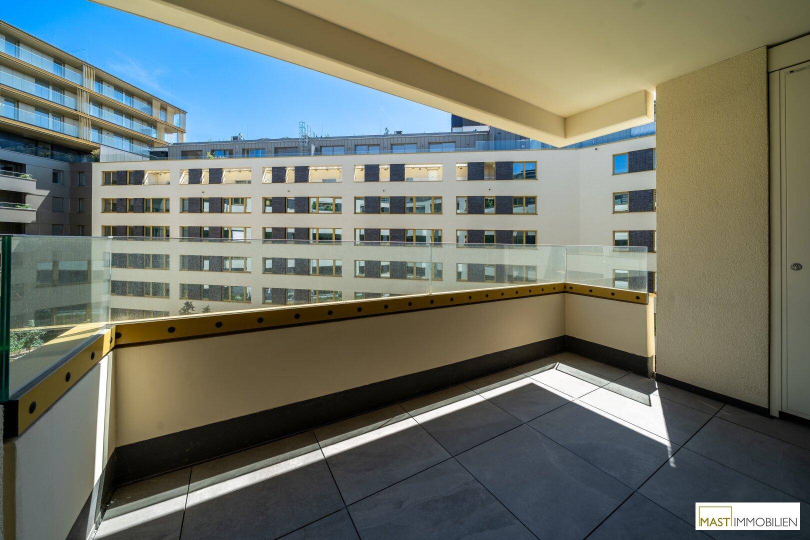 Sonniger Balkon mit Glasbrüstung und Blick auf die umliegenden modernen Gebäude.