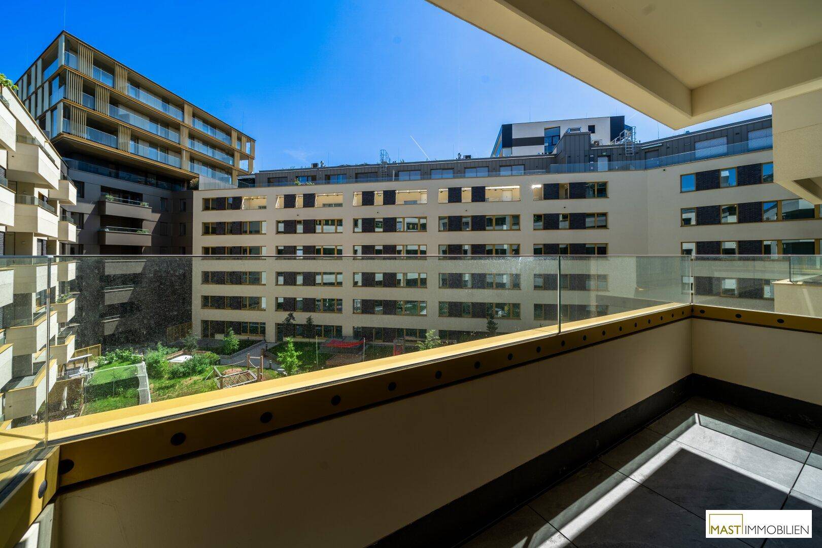 Balkon mit Blick auf die umliegenden modernen Gebäude und eine grüne Innenhofanlage.