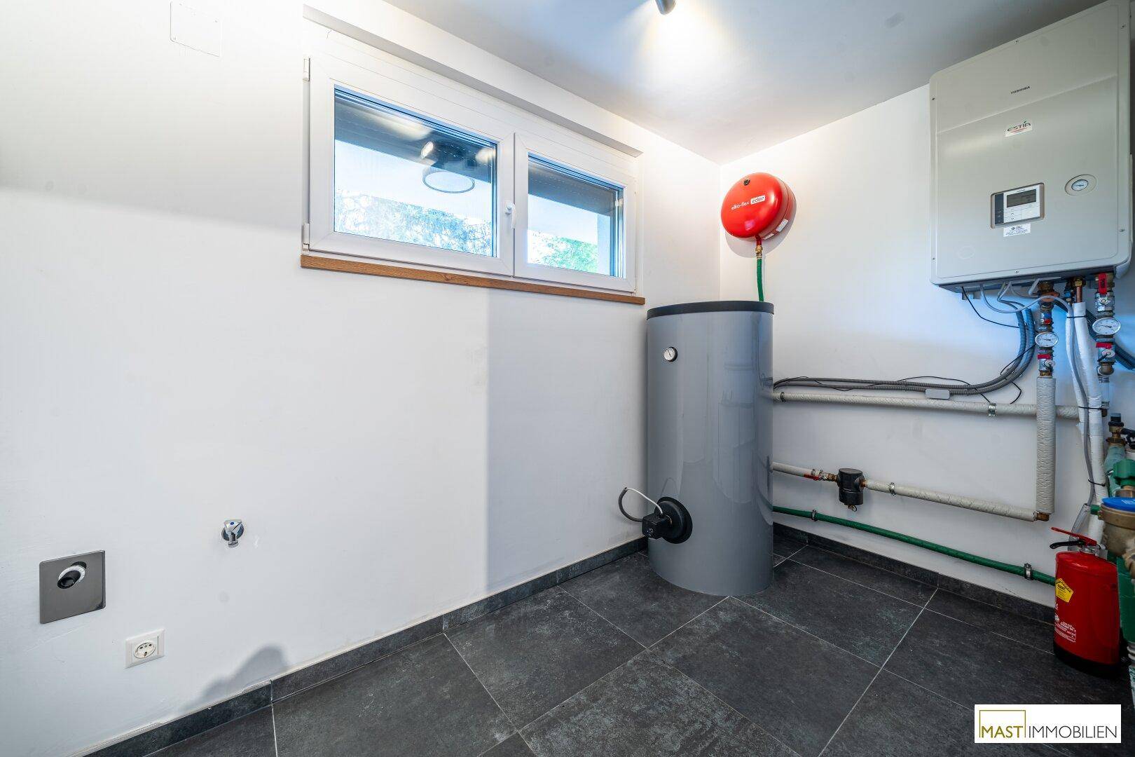 Funktionaler Hauswirtschaftsraum mit Warmwasserspeicher, Heizungsanlage und Fenster für Belüftung.