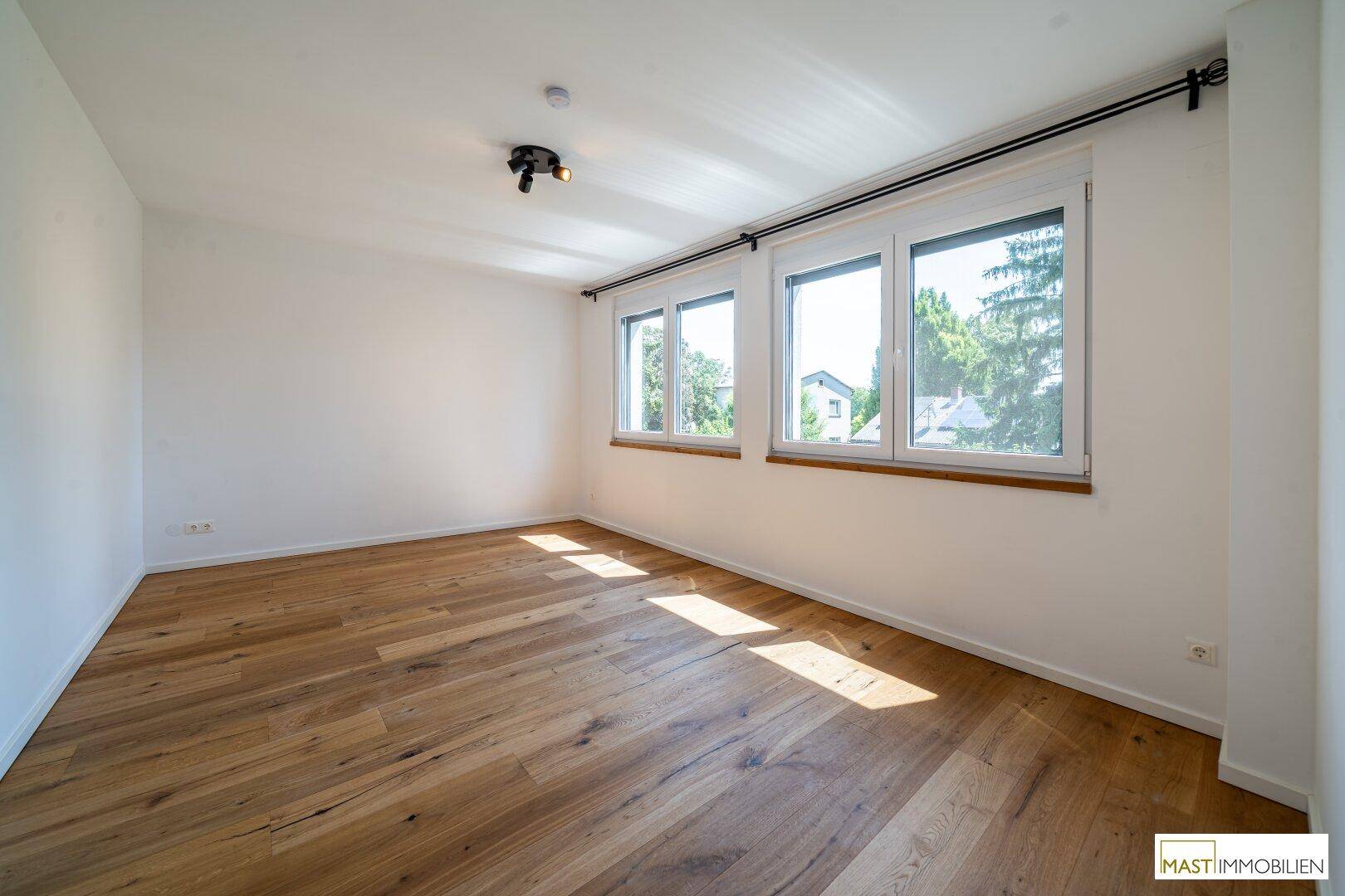 Geräumiges Schlafzimmer mit Holzparkett und großen Fenstern, die viel Tageslicht hereinlassen.