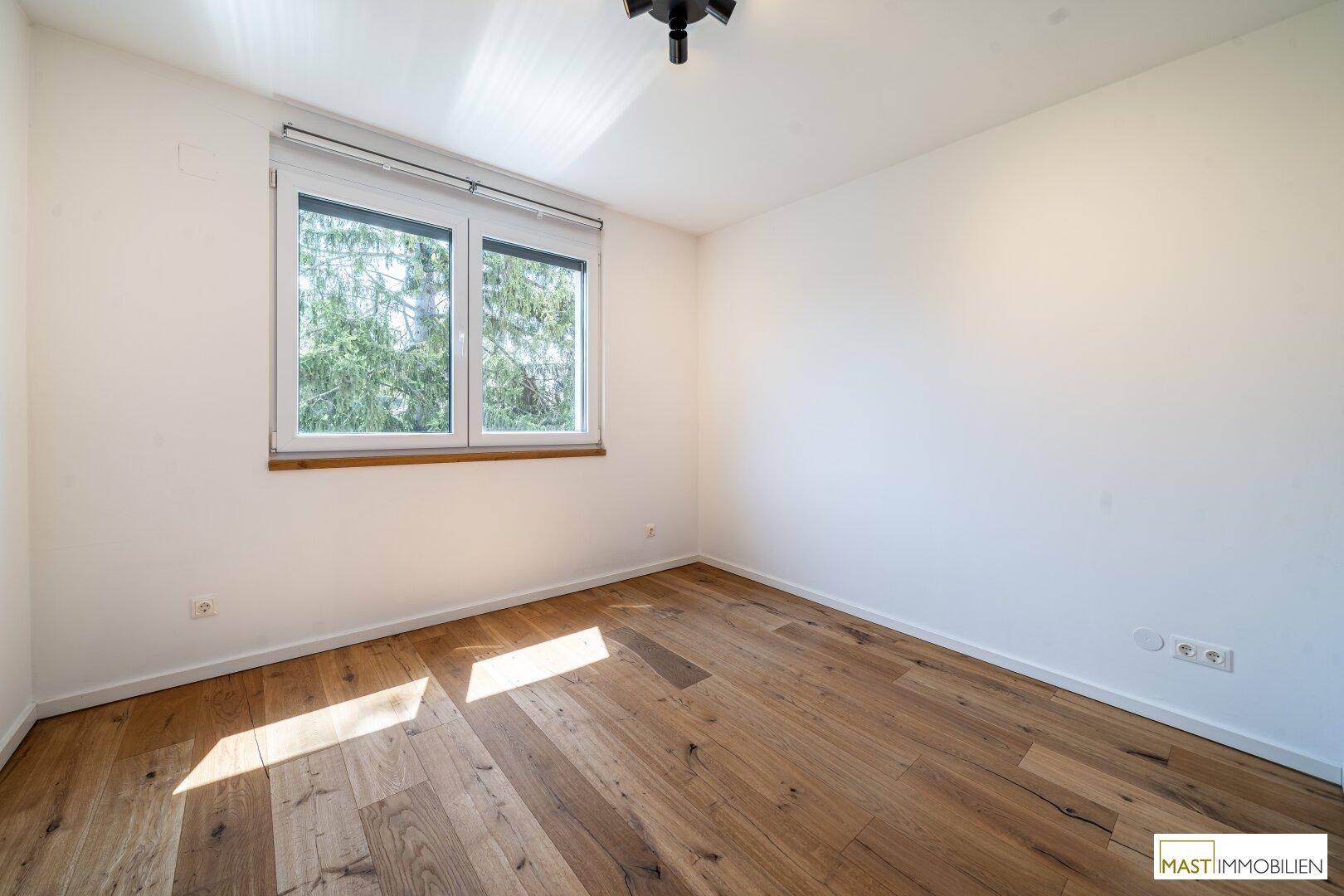 Gemütliches Schlafzimmer mit Holzparkettboden und einem Fenster, das für natürliche Belichtung sorgt.