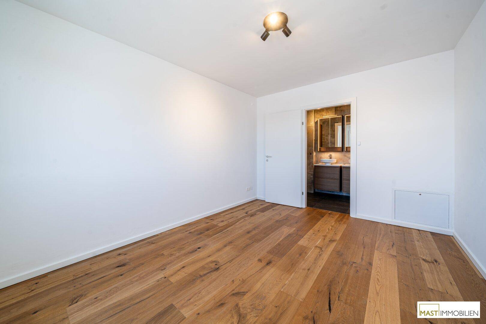 Helles Schlafzimmer mit Holzparkettboden und direktem Zugang zu einem modernen Badezimmer.