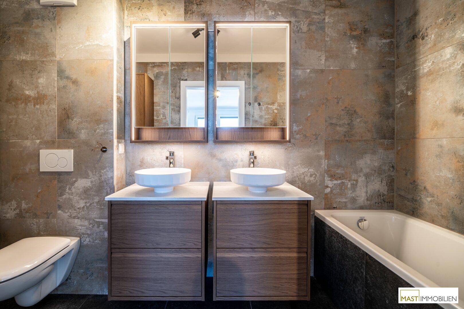 Modernes Badezimmer mit Doppelwaschbecken, zwei Spiegelschränken, WC und integrierter Badewanne.