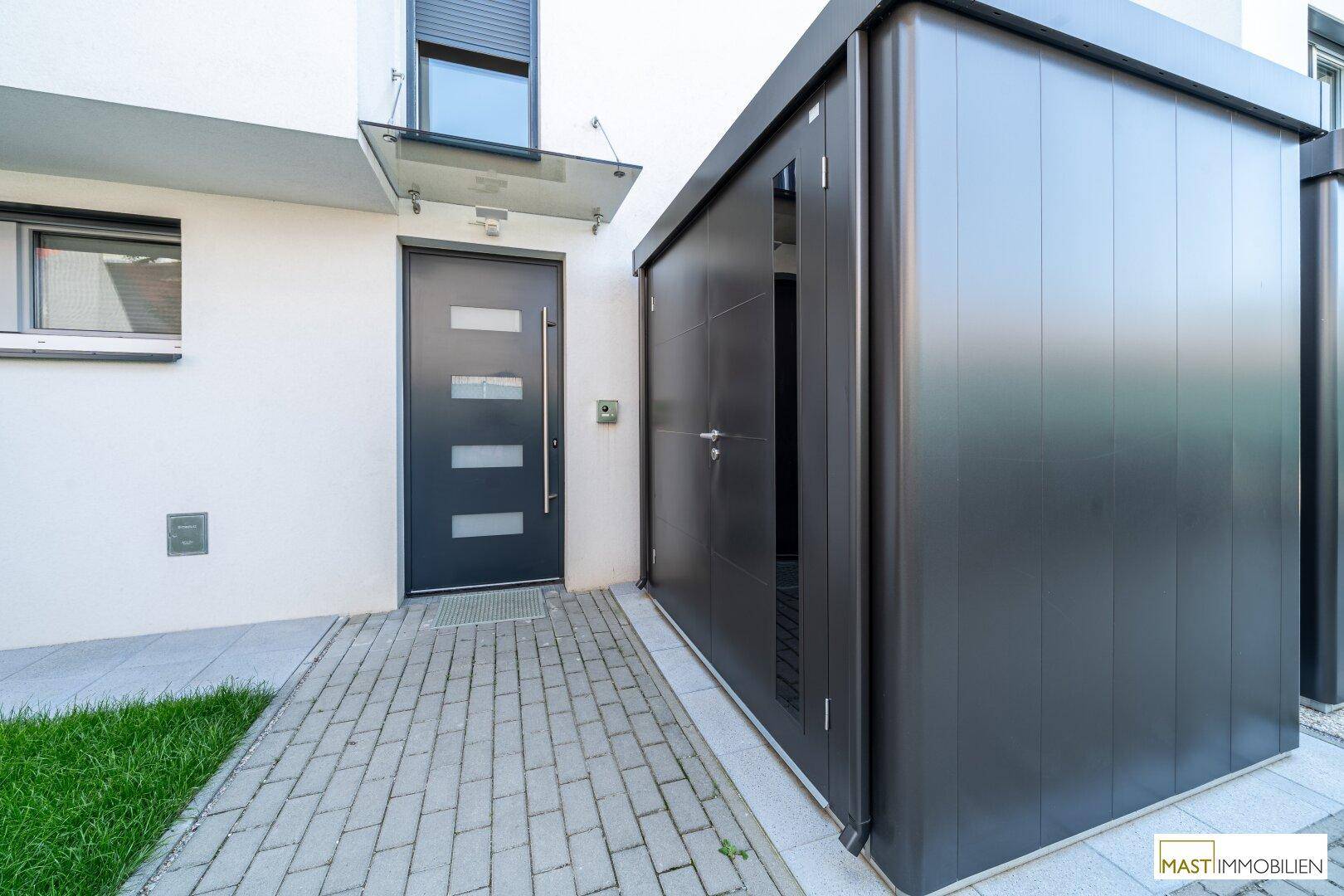 Moderner Hauseingang mit dunkler Tür und einem angrenzenden Carport oder Abstellraum.