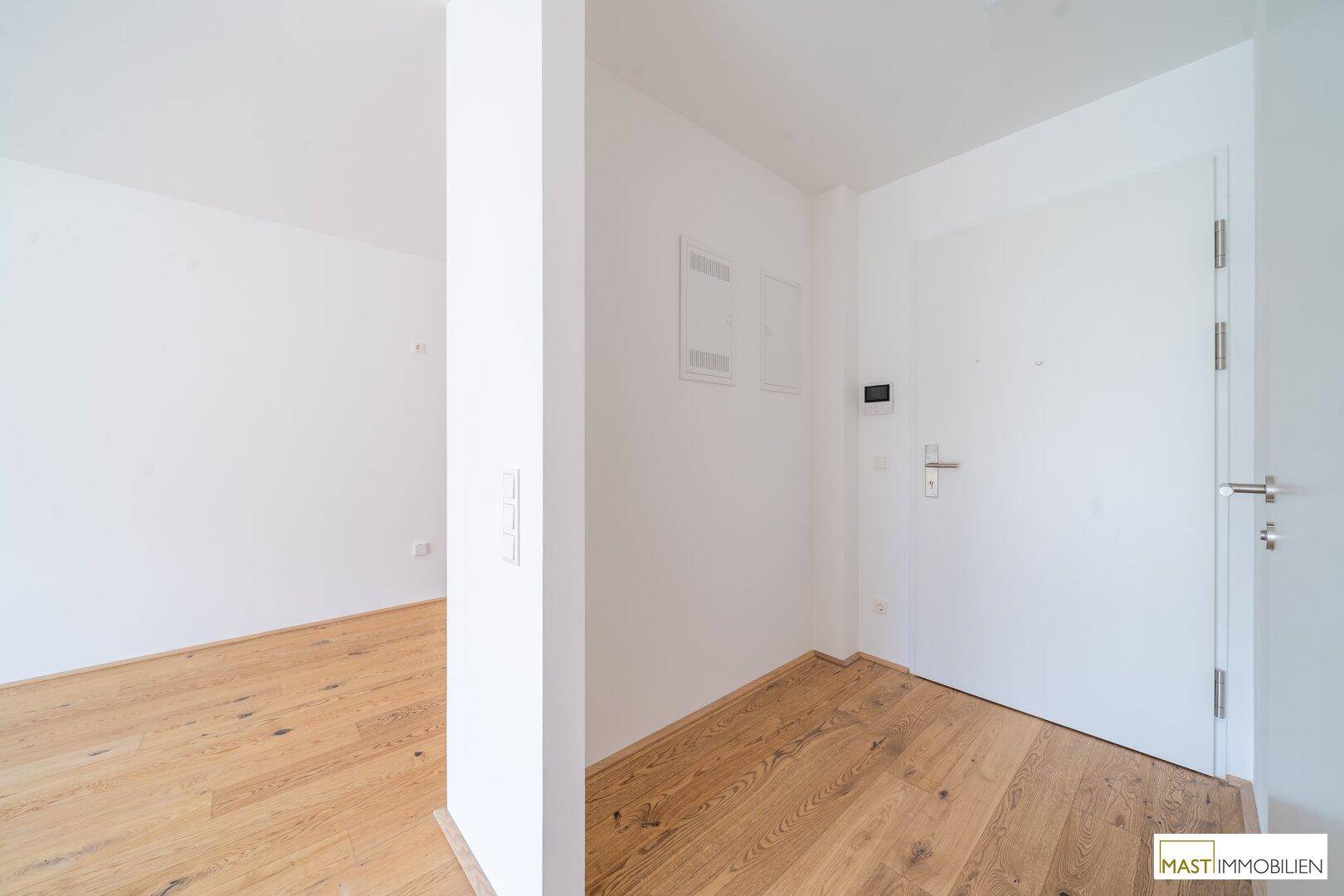 Heller Eingangsbereich mit Holzboden und weißer Tür, der zu den Wohnräumen führt.