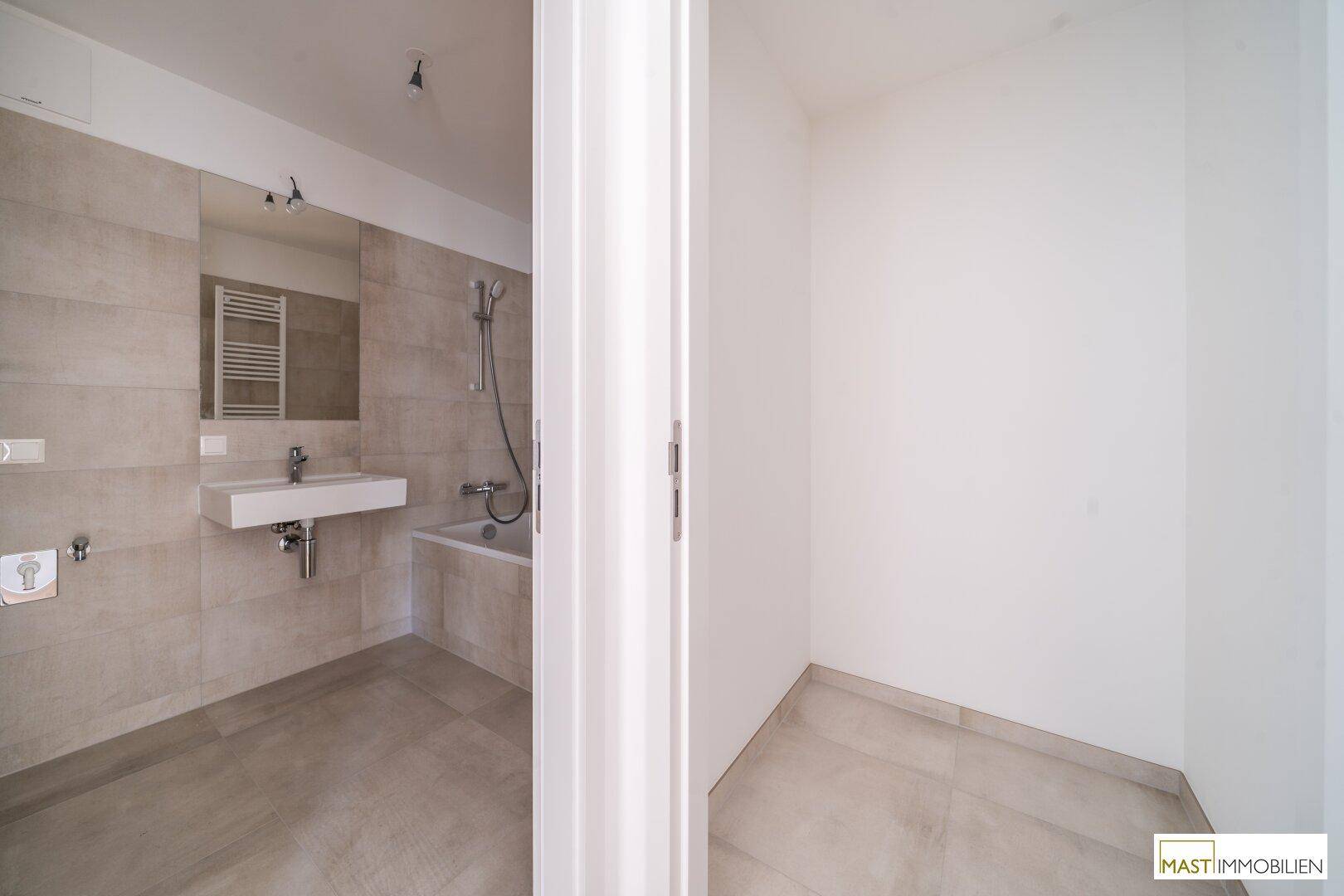 Modernes Badezimmer mit beigefarbenen Fliesen, Badewanne, Waschtisch und Spiegel.