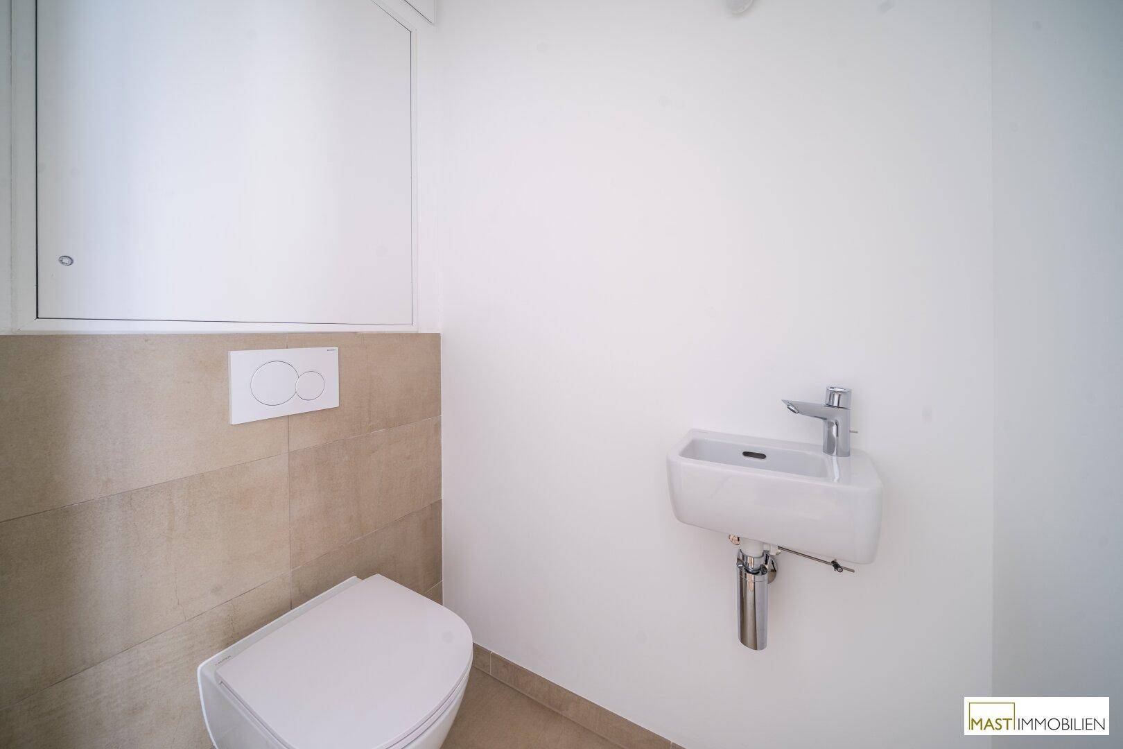 Modernes Gäste-WC mit wandhängendem WC und kleinem Waschbecken, teilweise mit beigen Fliesen.