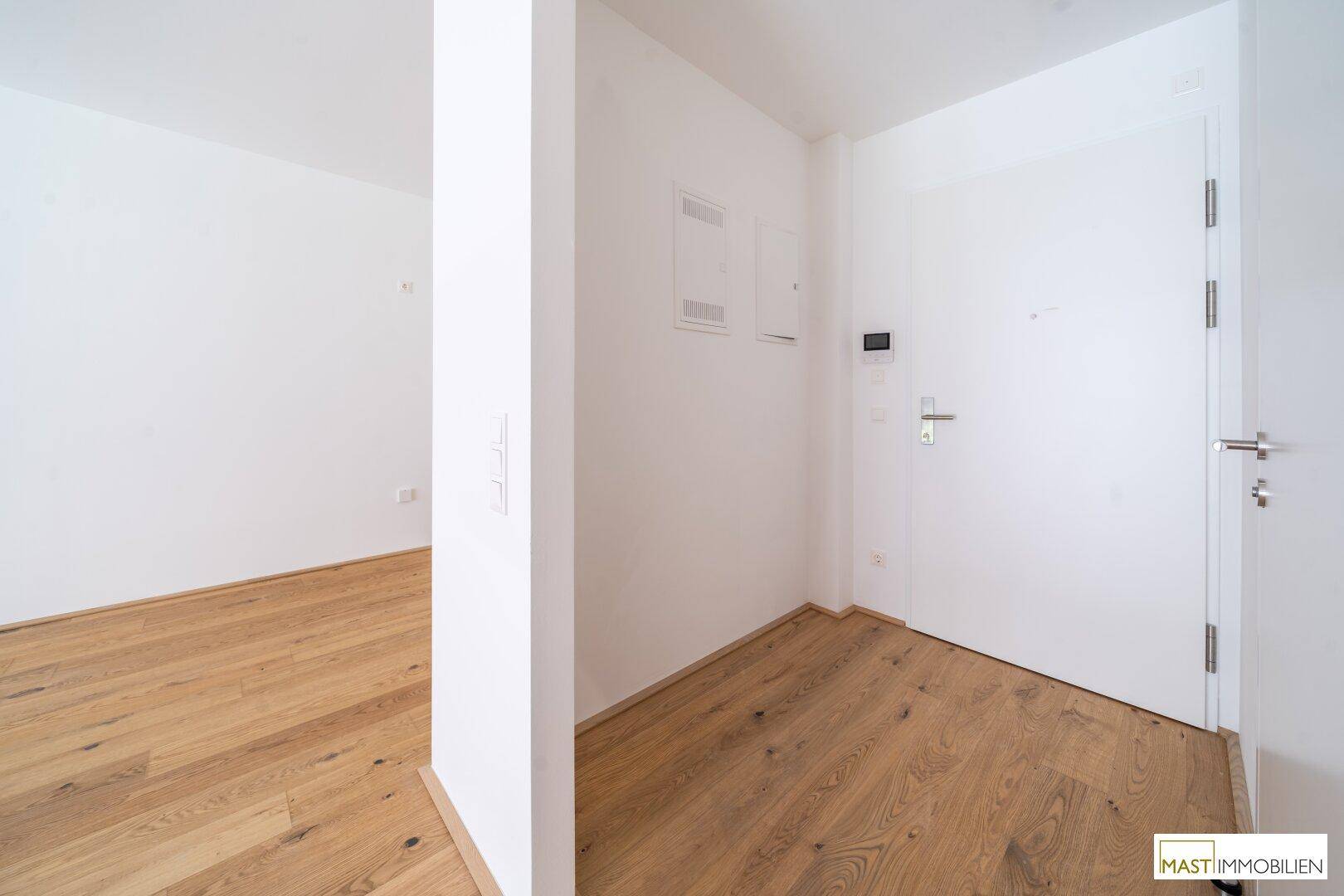 Heller Eingangsbereich mit Holzparkett und weißer Eingangstür in einem modernen Wohngebäude.