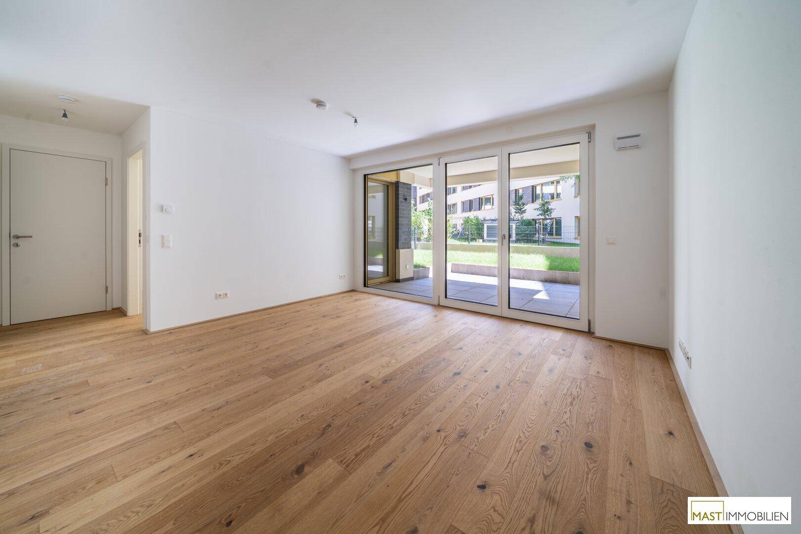 Heller, leerer Wohnraum mit Eichenparkett und großen Glasschiebetüren zur Terrasse und zum Garten.