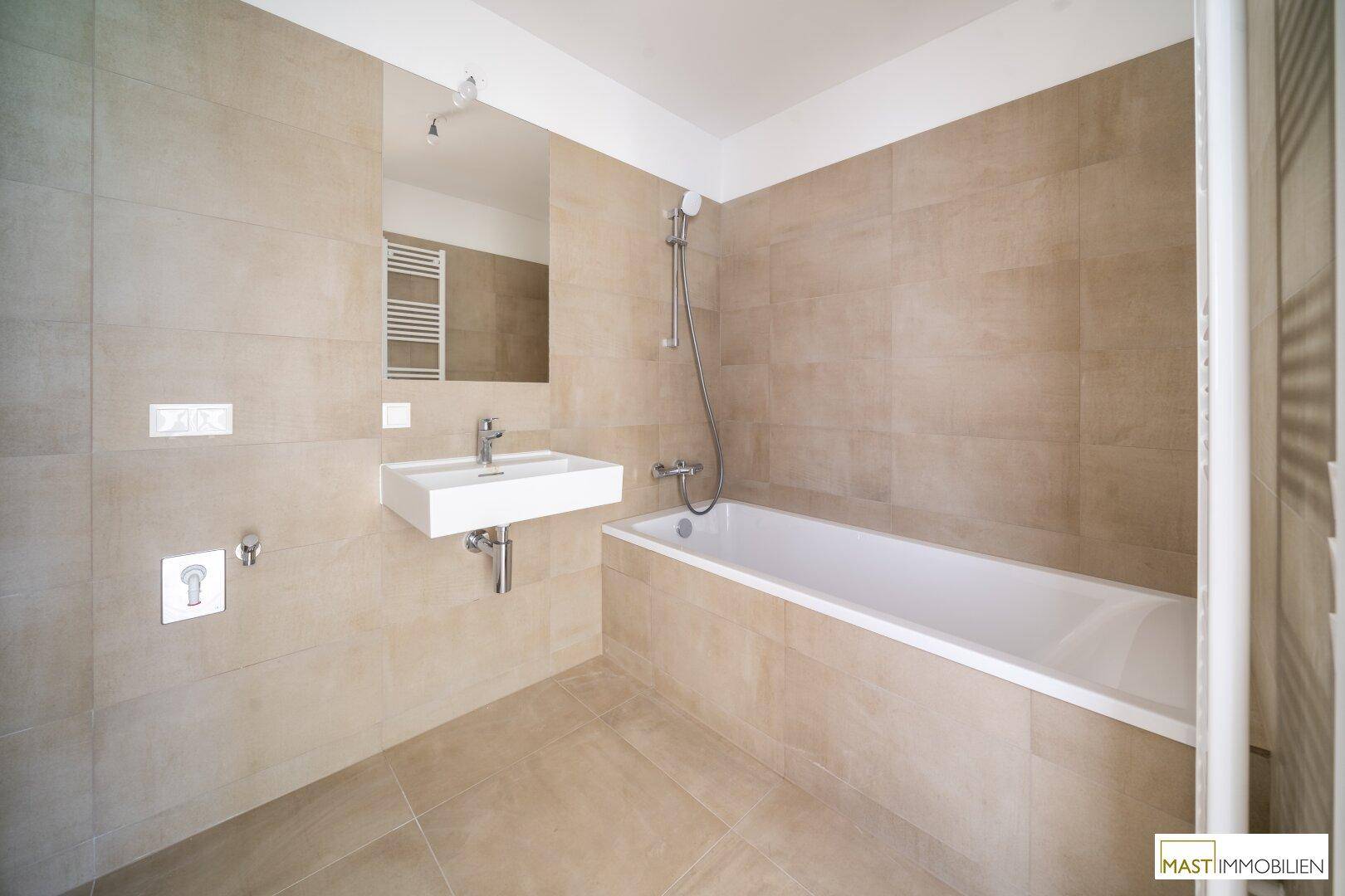 Modernes Badezimmer mit beigefarbenen Fliesen, Badewanne, wandmontiertem Waschbecken und Handtuchheizkörper.
