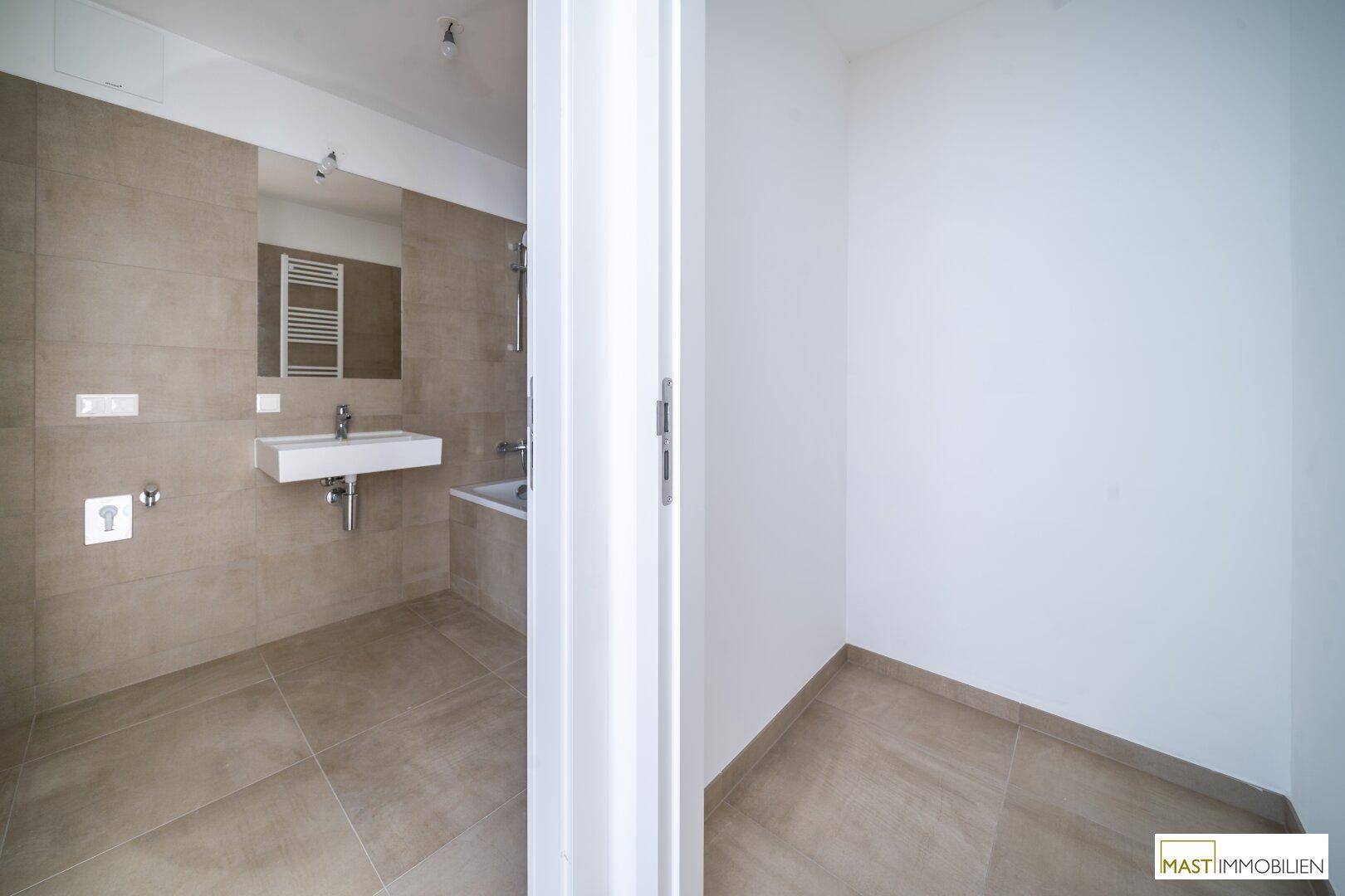 Blick durch eine Tür in ein modernes Badezimmer mit beigefarbenen Fliesen und einer Badewanne.