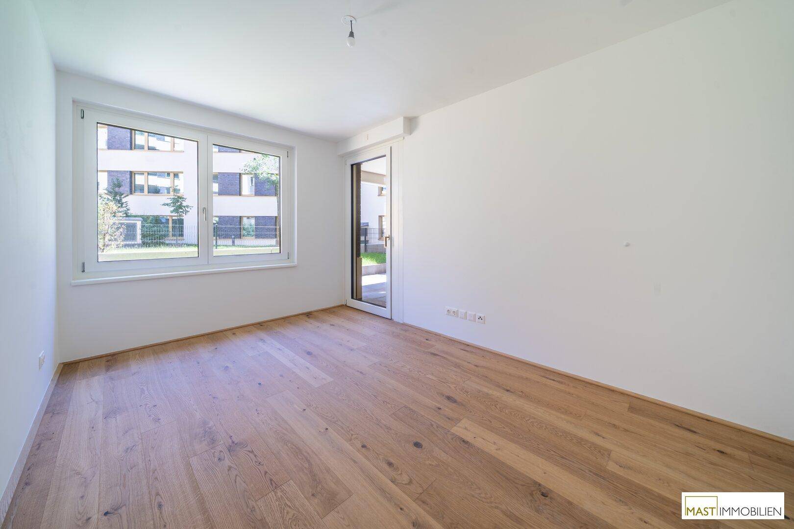 Helles Schlafzimmer mit Holzparkett, Fenster zum Innenhof und Zugang zu einem Außenbereich.