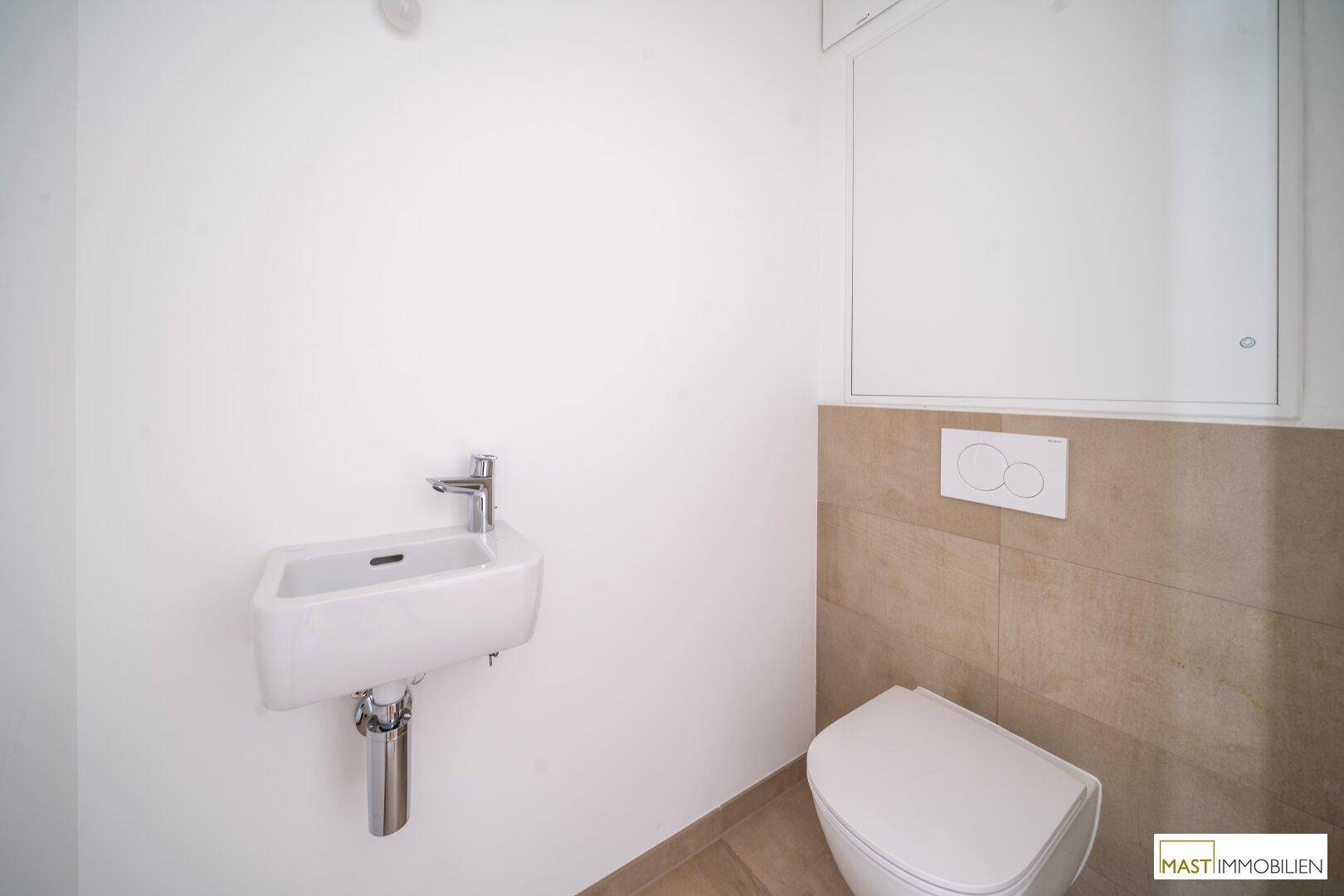 Modernes Gäste-WC mit wandhängender Toilette, kleinem Waschbecken und beigefarbenen Fliesen.