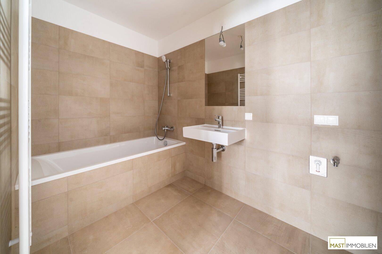 Modernes Badezimmer mit Badewanne, Duschfunktion, Waschbecken und großformatigen beigefarbenen Fliesen.