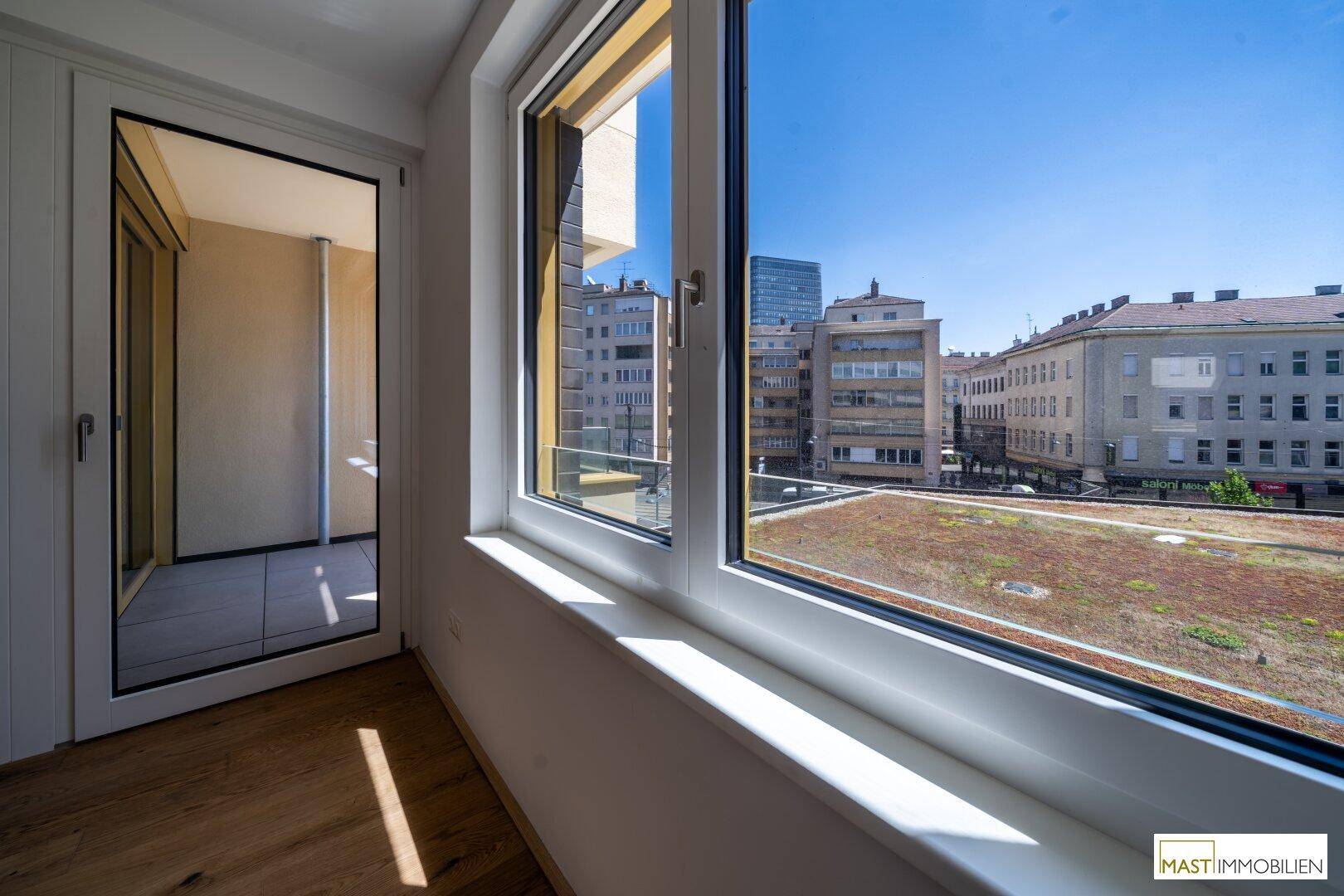 Blick aus dem Fenster auf eine städtische Umgebung mit begrüntem Dach und umliegenden Gebäuden.