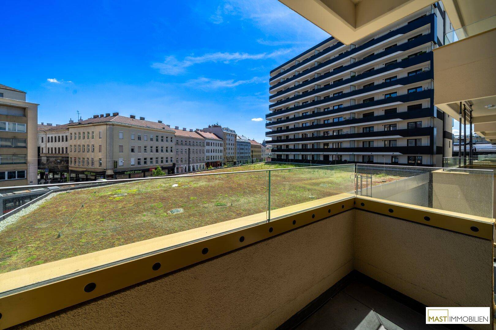 Weitläufiger Blick vom Balkon auf die moderne Architektur der Stadt und ein großes begrüntes Dach.