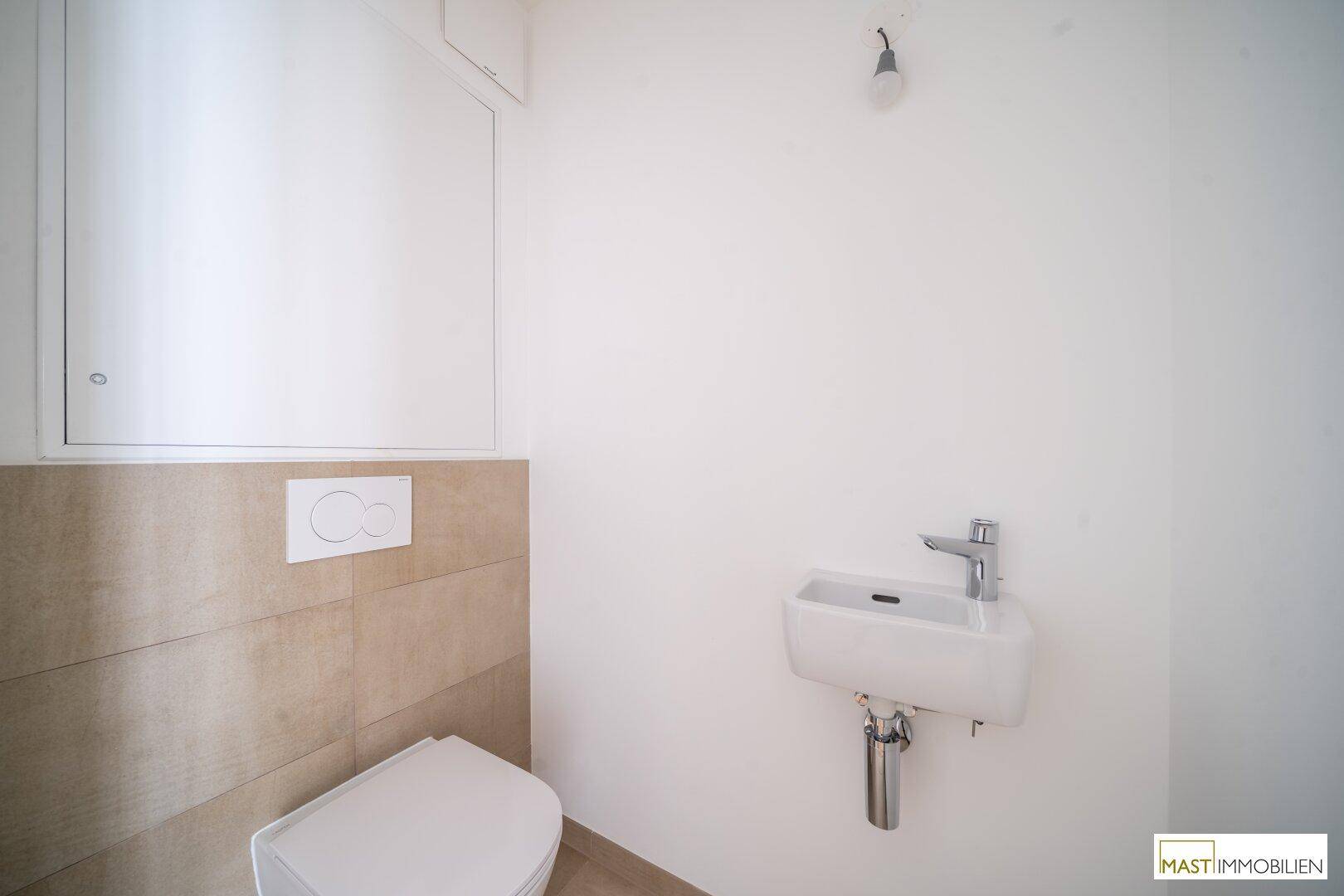 Gäste-WC mit wandhängender Toilette und kleinem Waschbecken, teilweise gefliest.