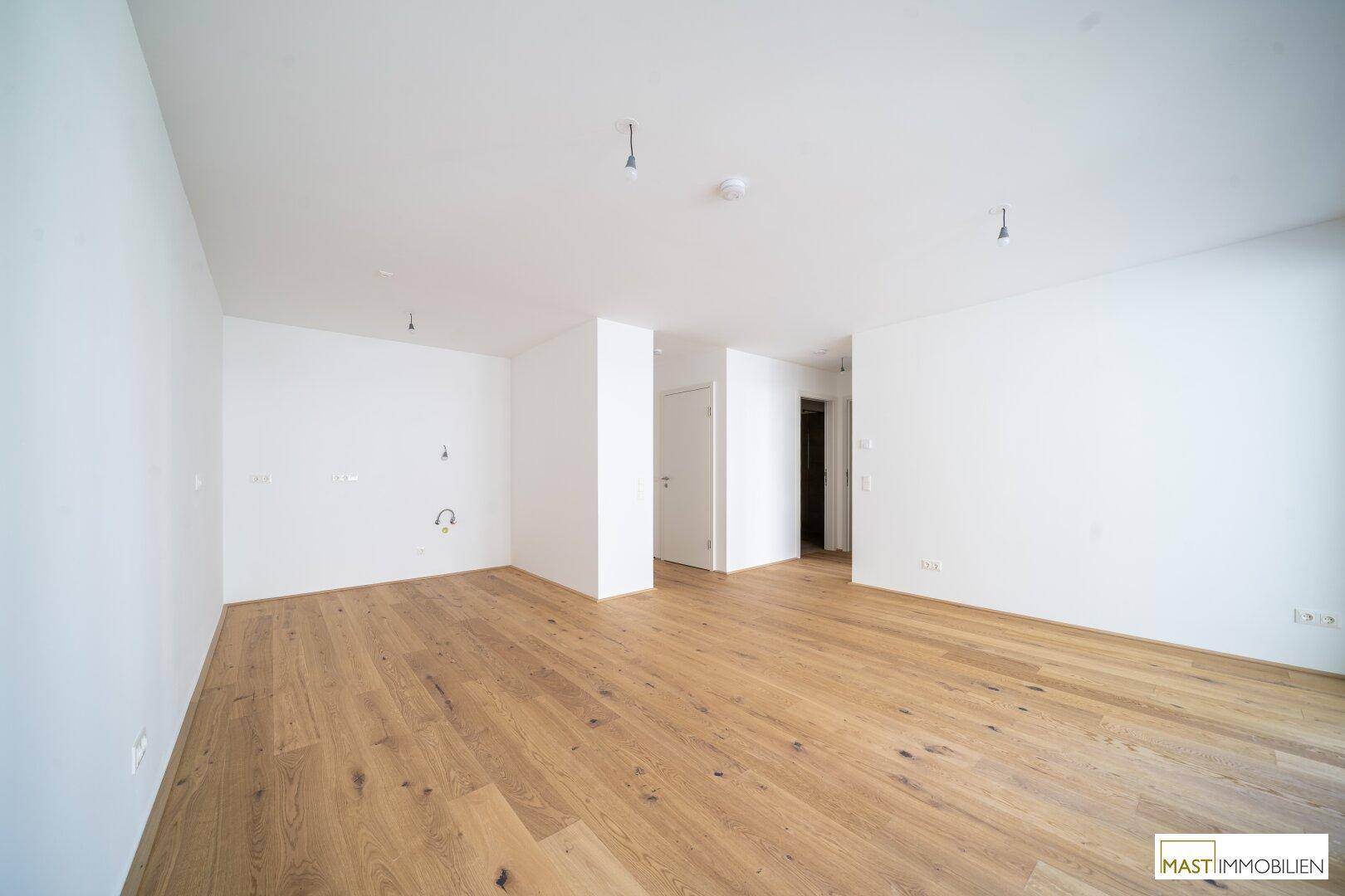 Leerer Raum mit Holzboden und Anschlüssen für eine zukünftige Küche.