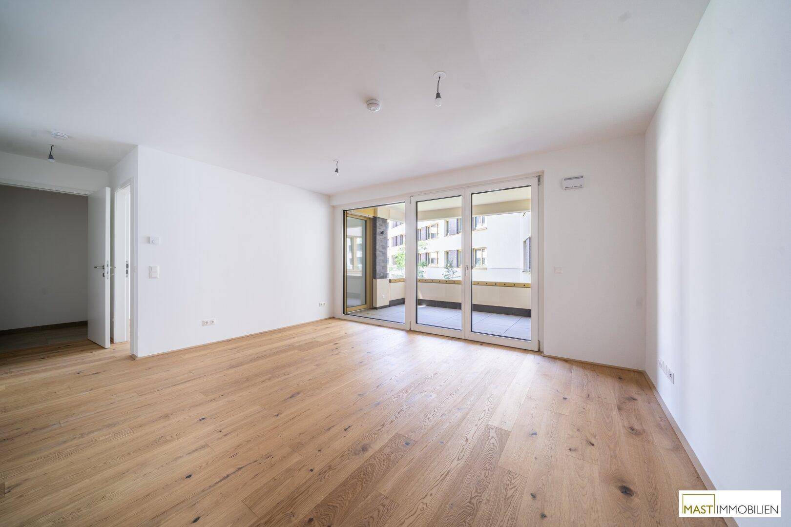 Geräumiger, heller Wohnbereich mit Holzboden und Zugang zu einem Balkon.