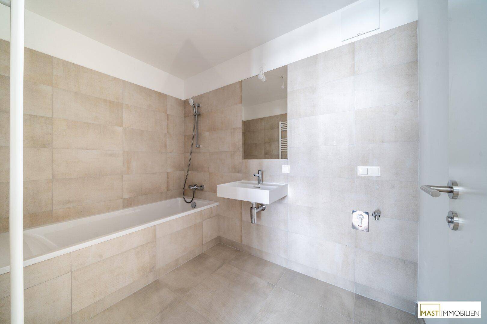 Modernes Badezimmer mit beigefarbenen Fliesen, Badewanne und einem einzelnen Waschbecken.