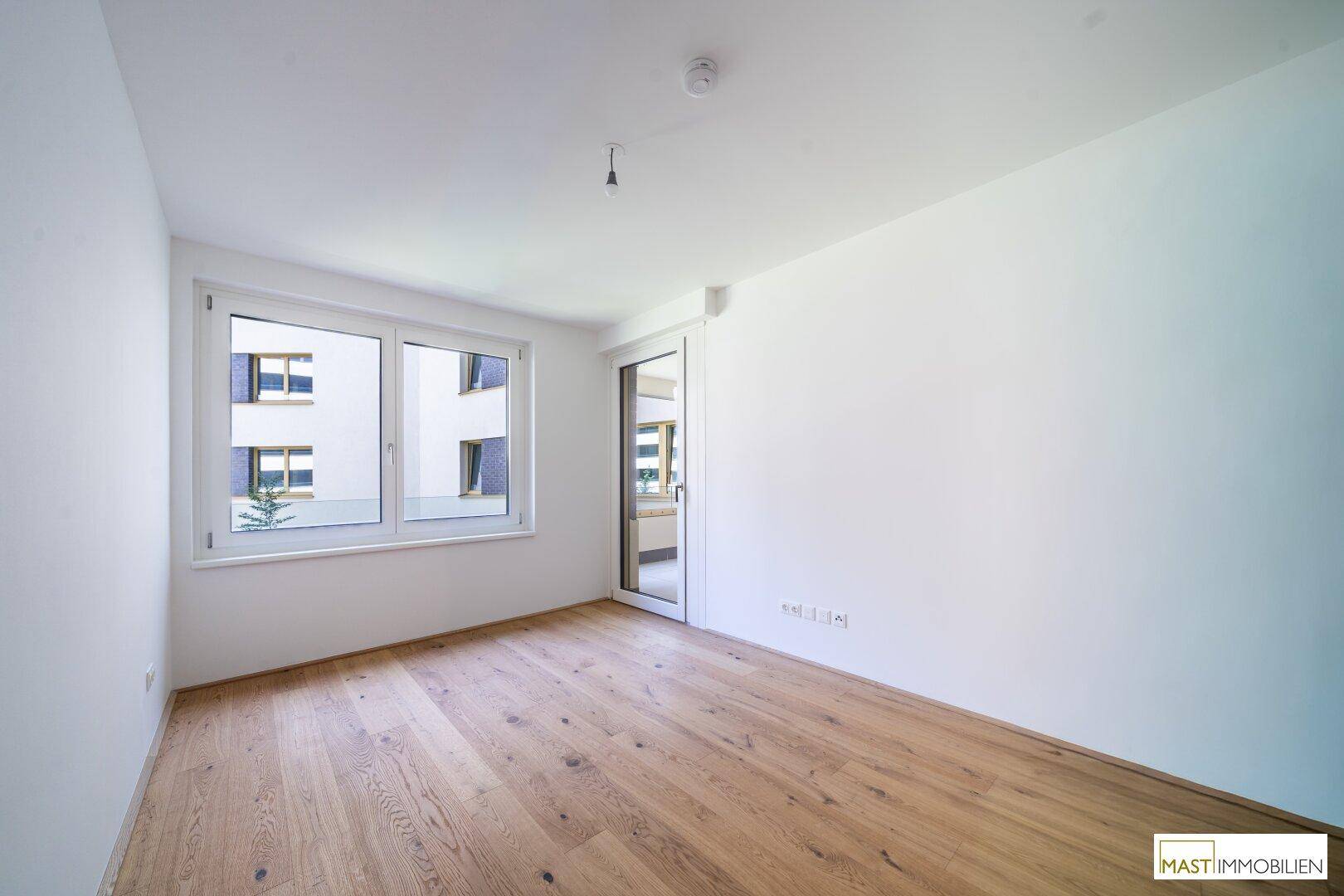 Helles Zimmer mit Holzboden und großem Fenster, das viel Tageslicht hereinlässt.