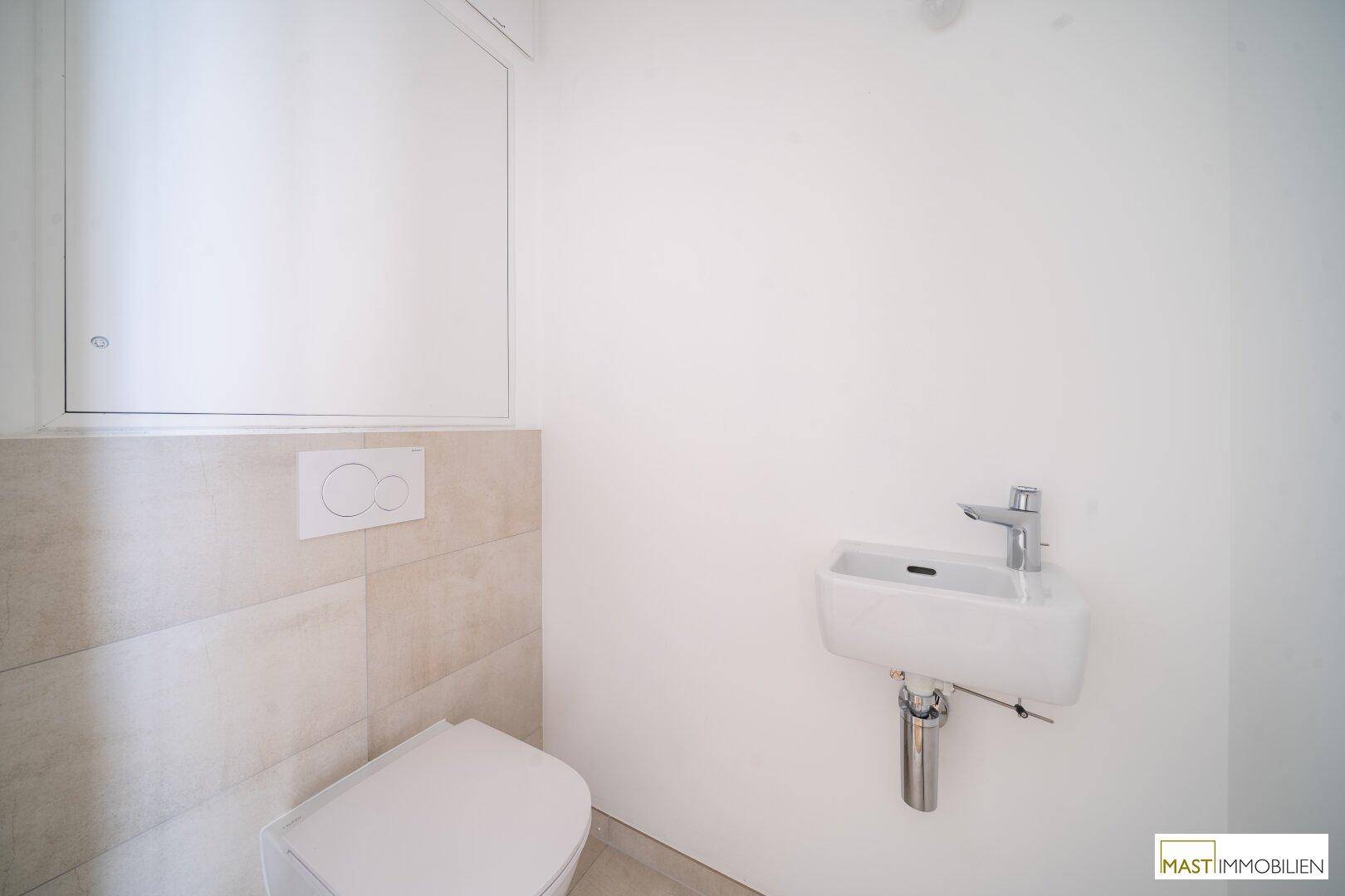 Separates WC mit wandhängender Toilette und kleinem Handwaschbecken, in modernem Design.