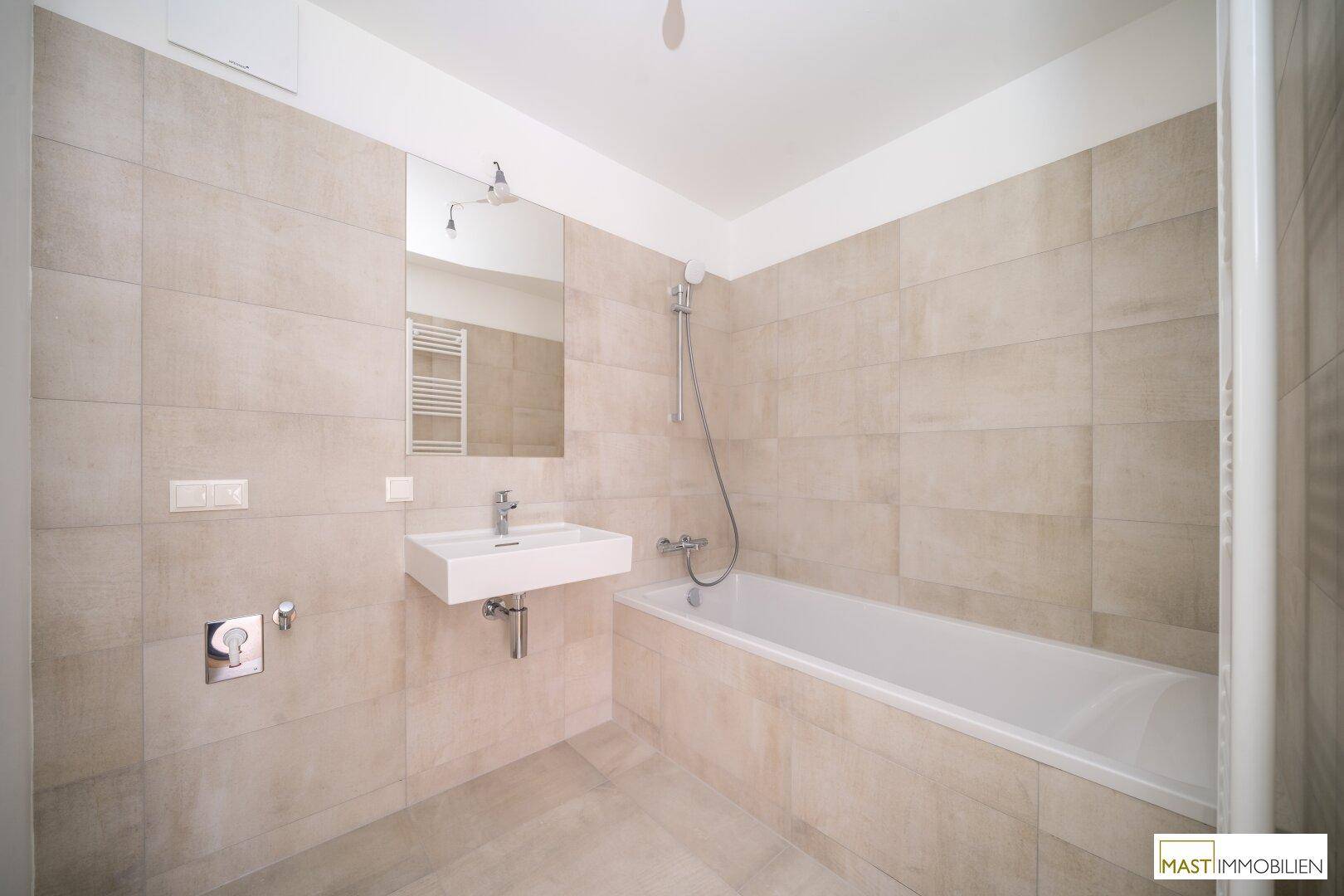 Modernes Badezimmer mit Badewanne, Waschbecken und beigefarbenen Fliesen an Wänden und Boden.