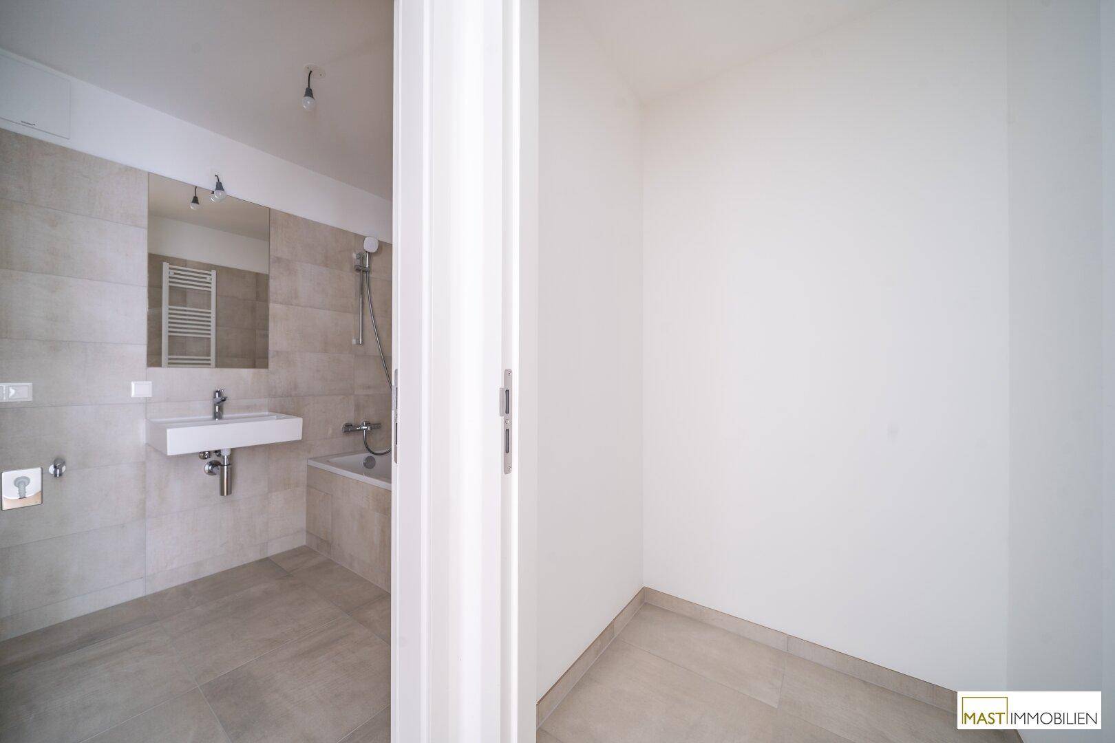 Modernes Badezimmer mit Badewanne und Waschbecken, angrenzend an einen kleinen Abstellraum.