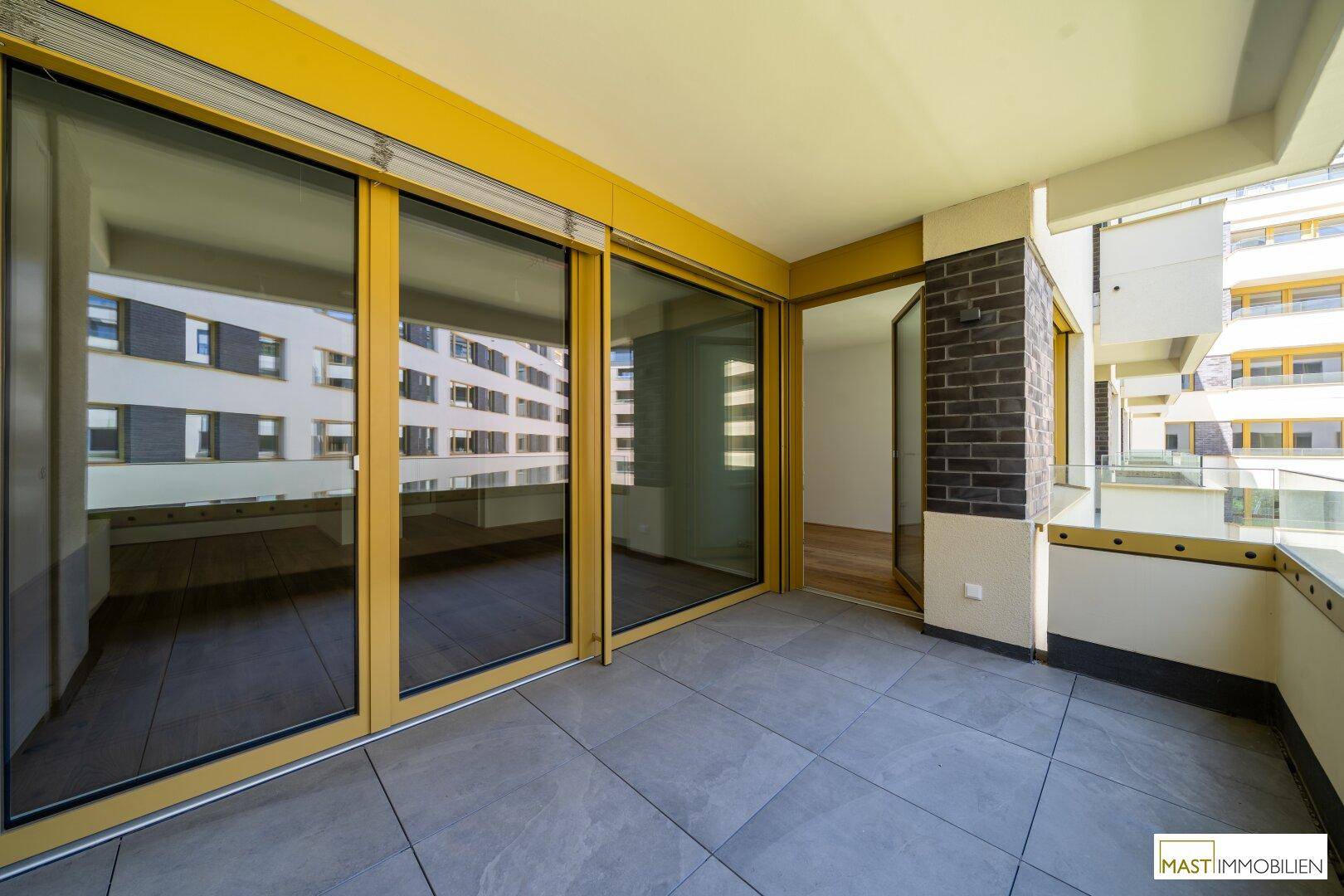 Geräumiger Balkon mit Fliesenboden und großen Schiebetüren, bietet viel Tageslicht und Ausblick.