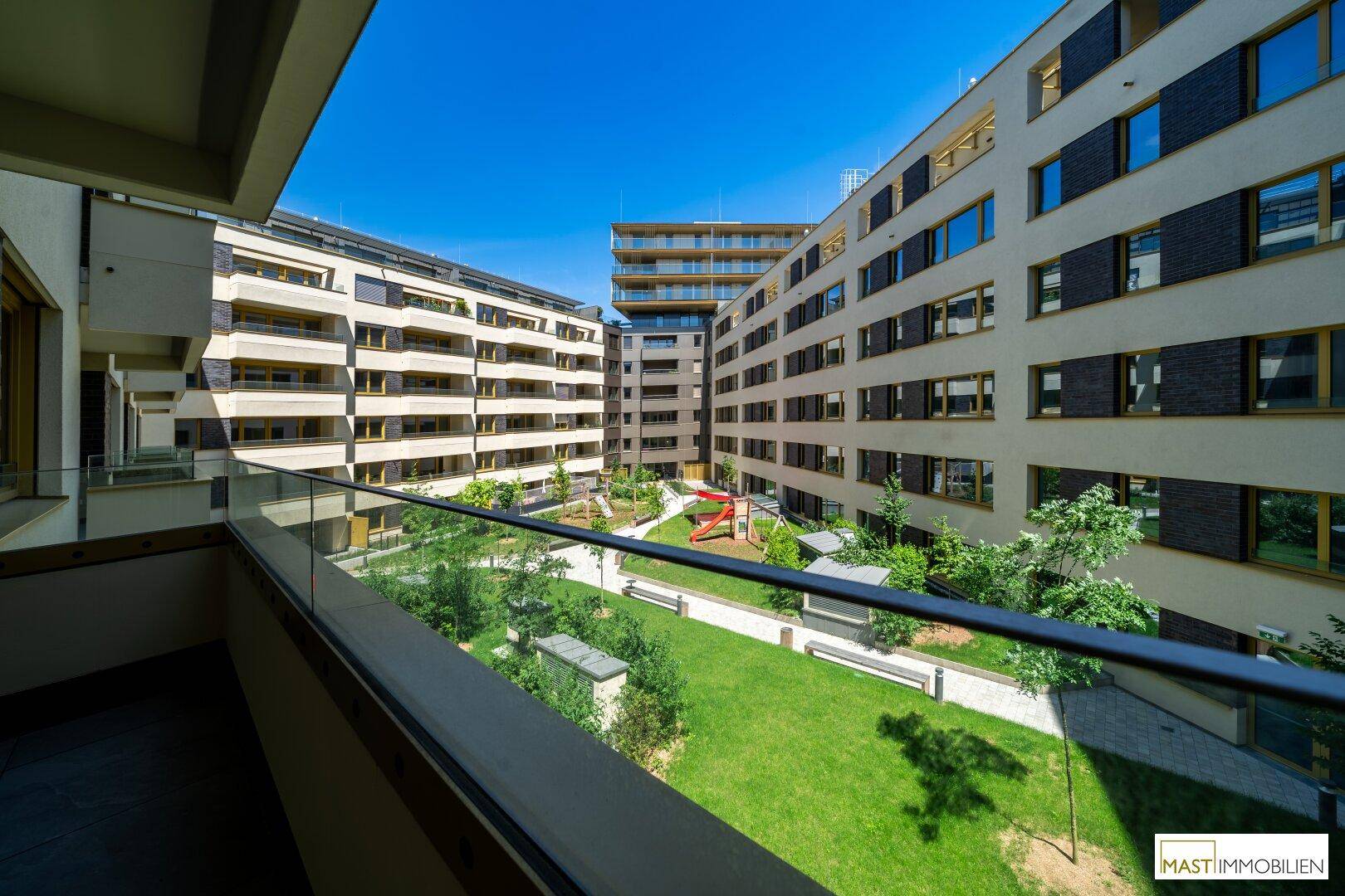 Balkon mit Blick auf den begrünten Innenhof und die umliegenden modernen Wohngebäude mit Spielplatz.