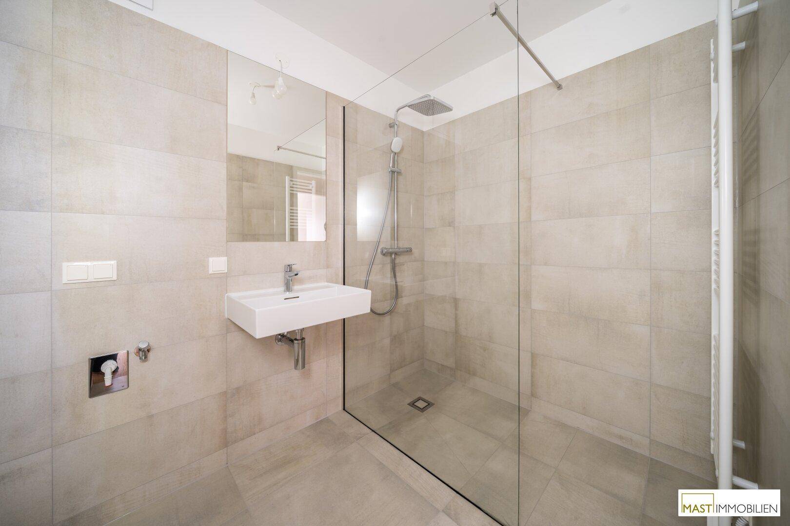 Elegantes Badezimmer mit großer begehbarer Dusche, modernem Waschbecken und beheiztem Handtuchhalter.
