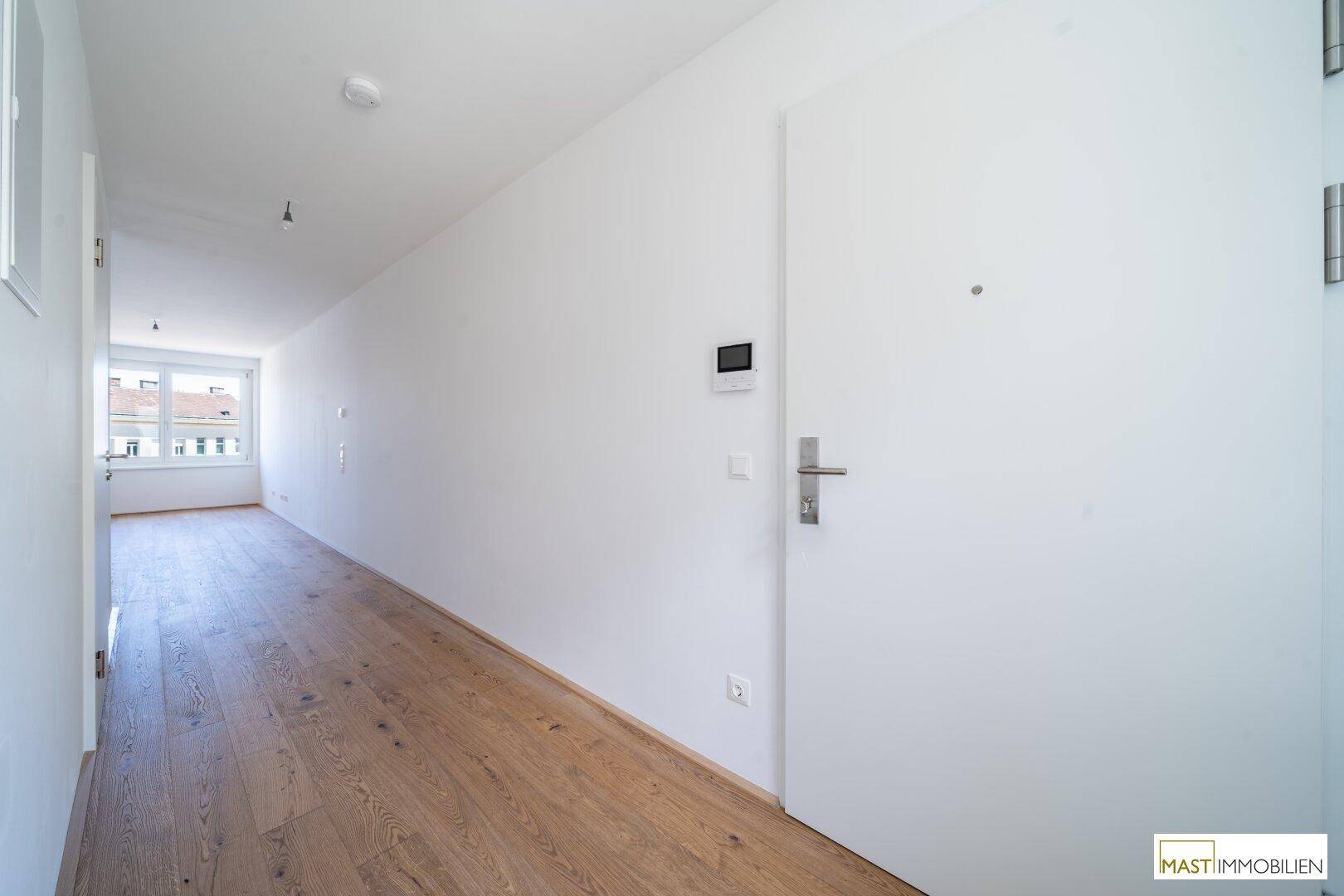 Heller Eingangsbereich mit Parkettboden und moderner Wohnungstür.
