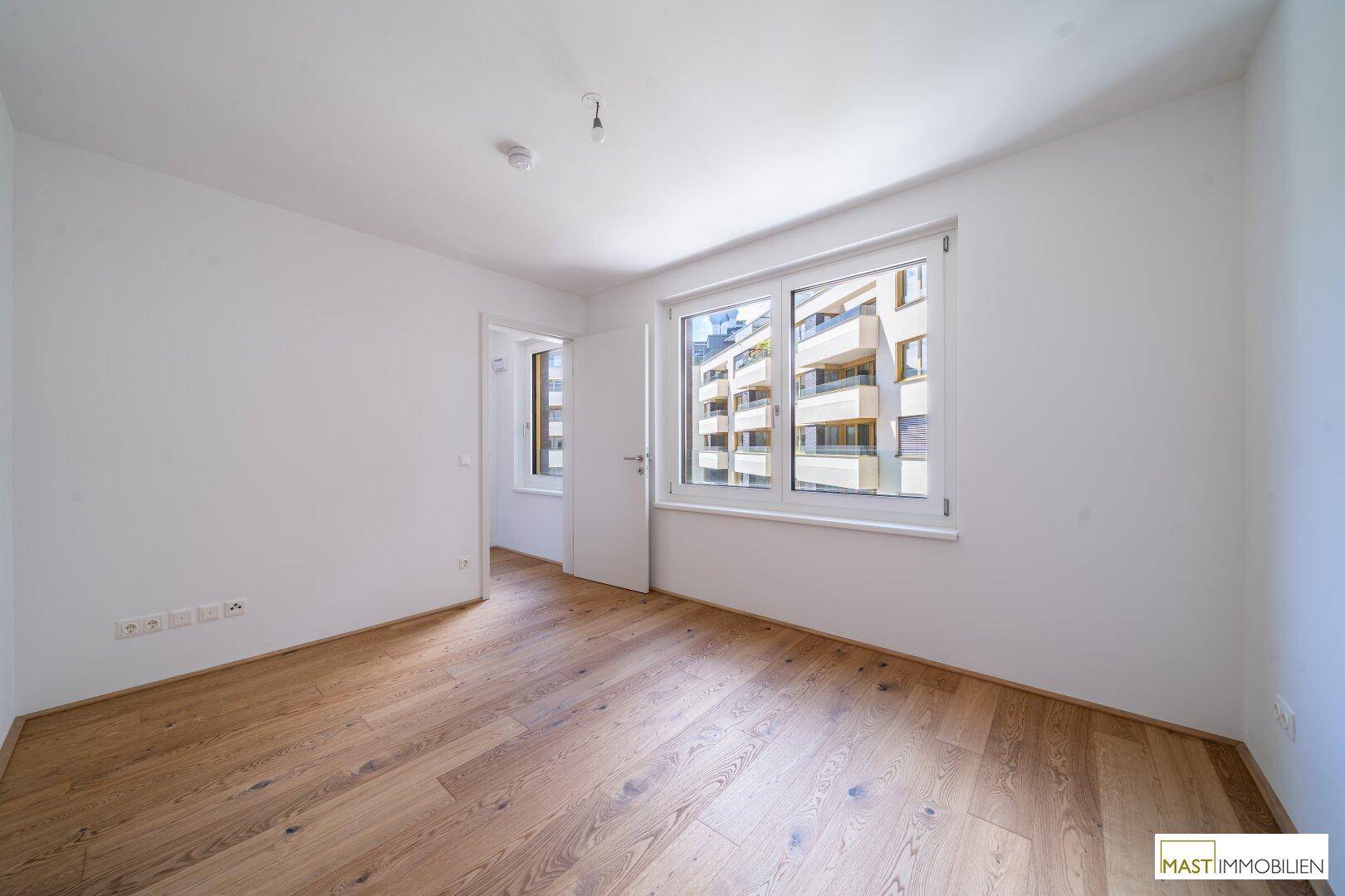 Helles Schlafzimmer mit Parkettboden und Blick auf die umliegenden Gebäude.