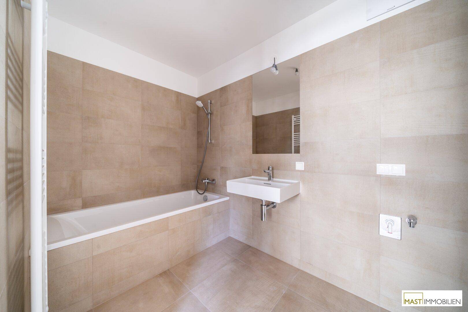Modernes Badezimmer mit Badewanne, Waschbecken und beigefarbenen Fliesen.