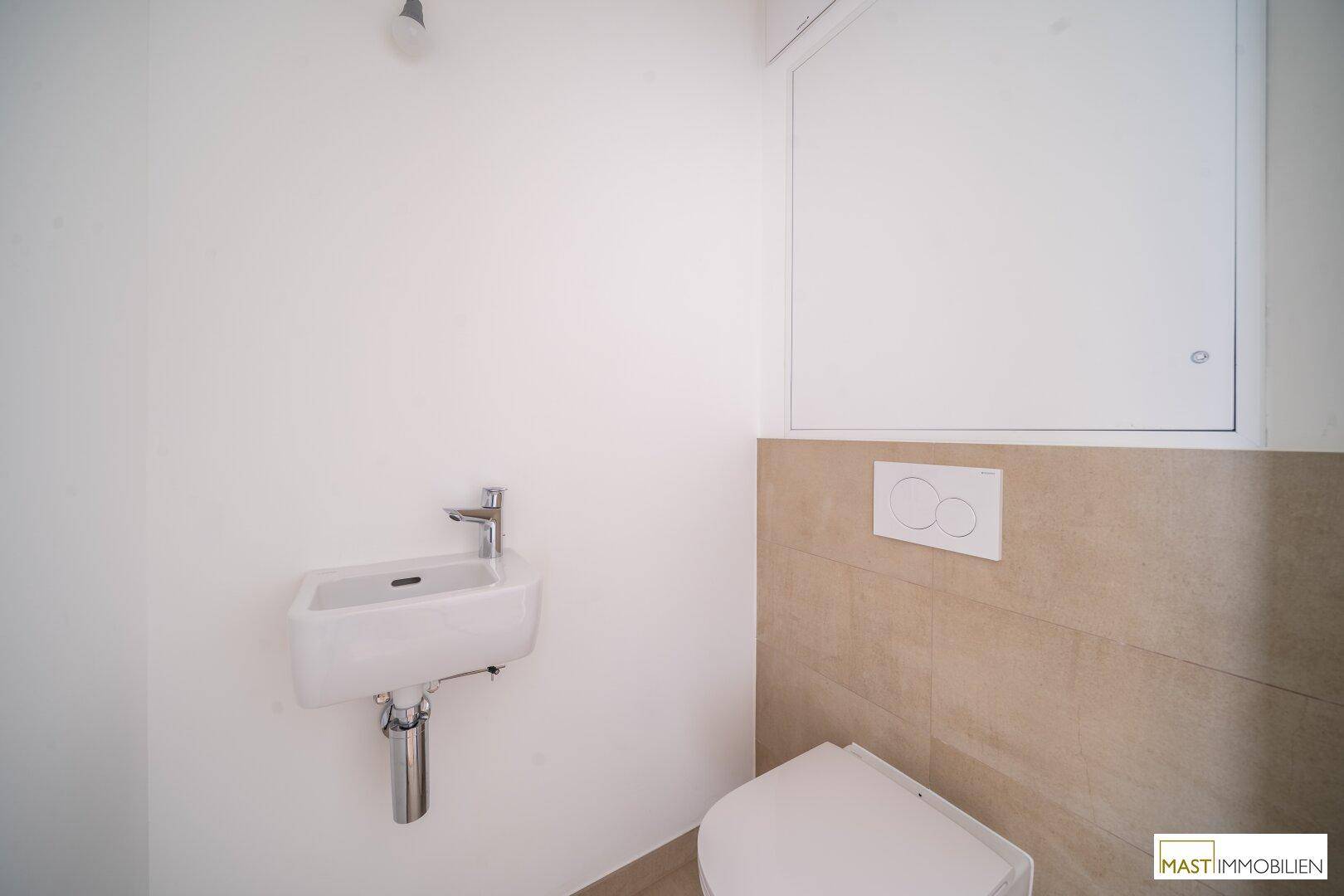 Modernes Gäste-WC mit wandhängender Toilette, kleinem Waschbecken und beigefarbenen Fliesen.