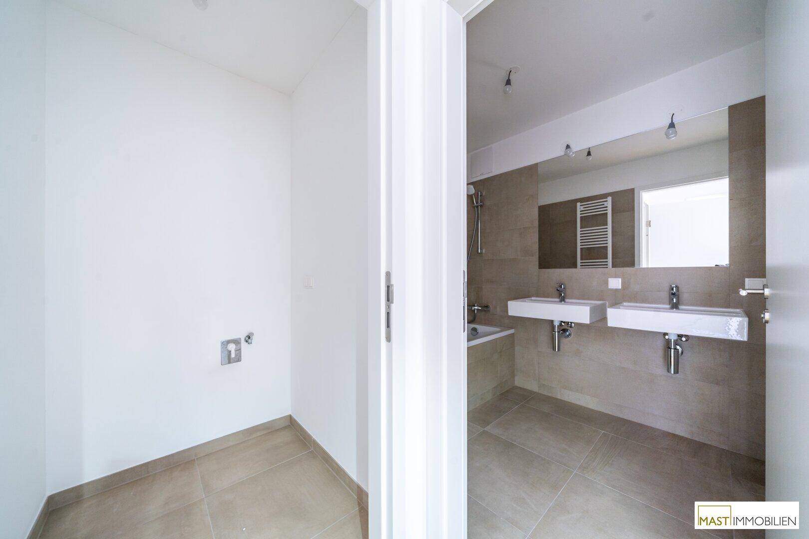Badezimmer mit Platz für Waschmaschine und Blick auf Doppelwaschbecken und großen Spiegel.