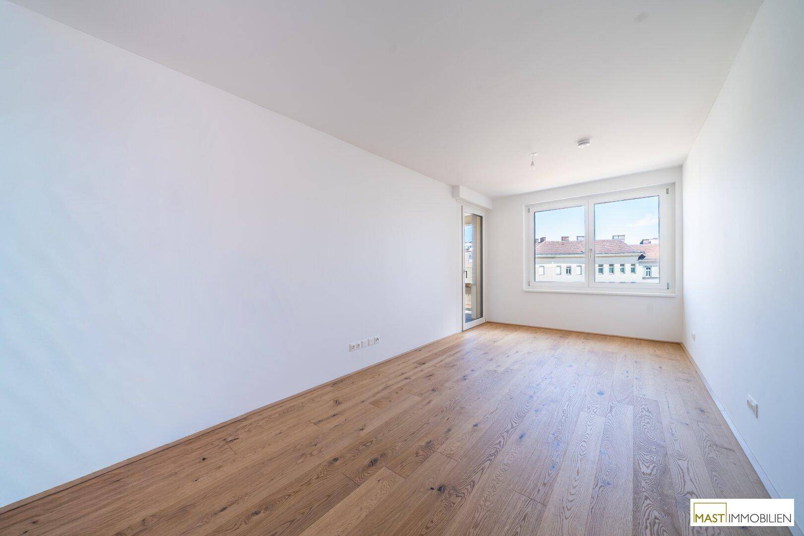 Helles Schlafzimmer mit Parkettboden und großem Fenster, das viel natürliches Licht hereinlässt.