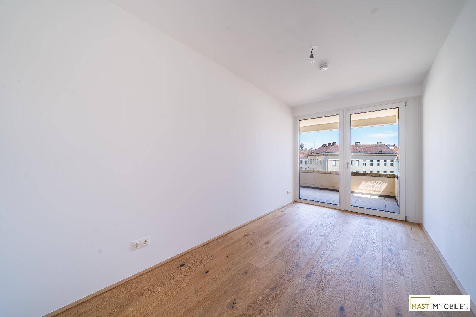 Helles Schlafzimmer mit Parkettboden und großem Fenster, das Zugang zu einem Balkon bietet.
