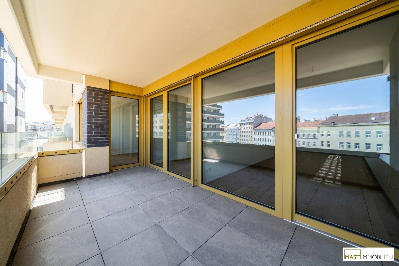 Großer, gefliester Balkon mit raumhohen Glasfronten, die viel Tageslicht in die Innenräume lassen.