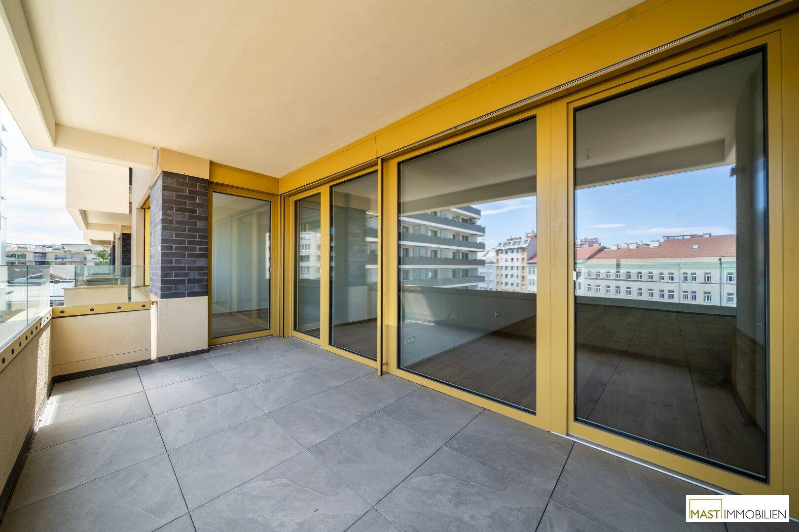Geräumiger Balkon mit Fliesenboden und gelben Fensterrahmen, bietet einen Blick auf die Umgebung.