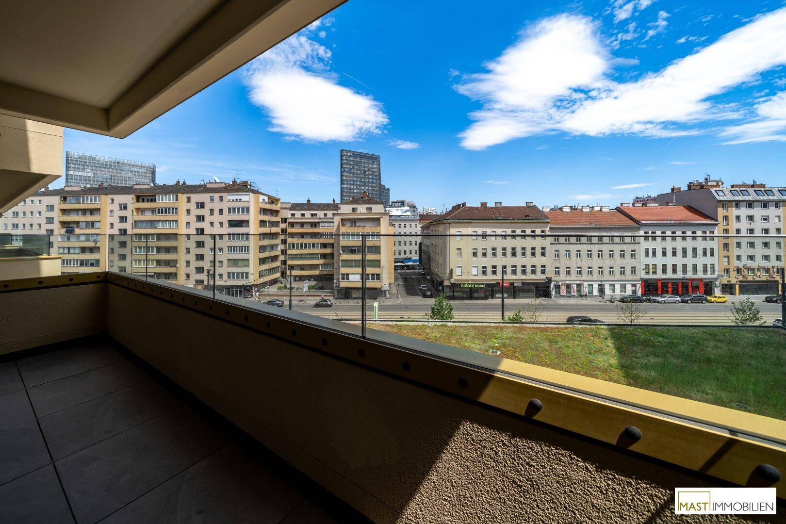 Weitläufiger Blick vom Balkon auf die Stadtlandschaft mit Gebäuden und einer belebten Straße.