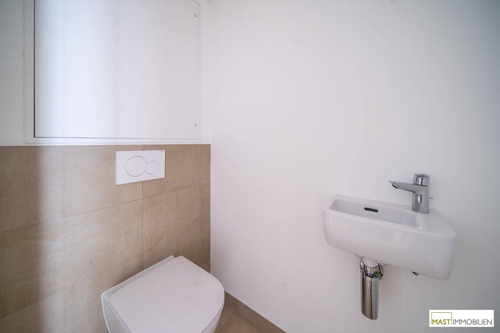 Kleines Gäste-WC mit modernen beigen Fliesen, einer Toilette und einem Handwaschbecken.