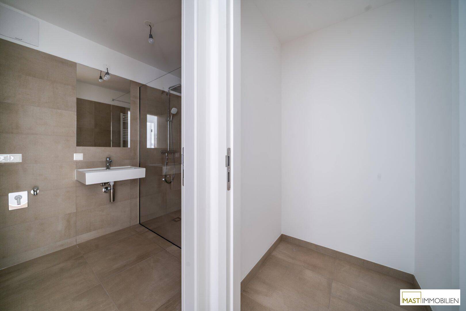 Badezimmer mit moderner Dusche und Waschtisch, durch eine Tür vom Flur getrennt.