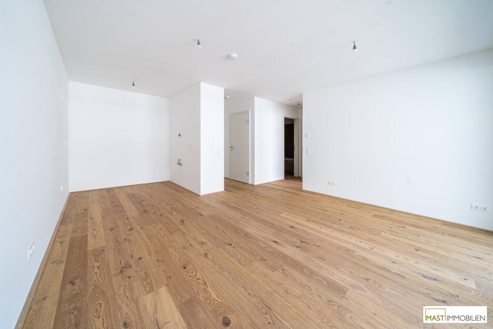 Geräumiges, leeres Zimmer mit hellem Holzboden und weißen Wänden, bereit zur individuellen Gestaltung.