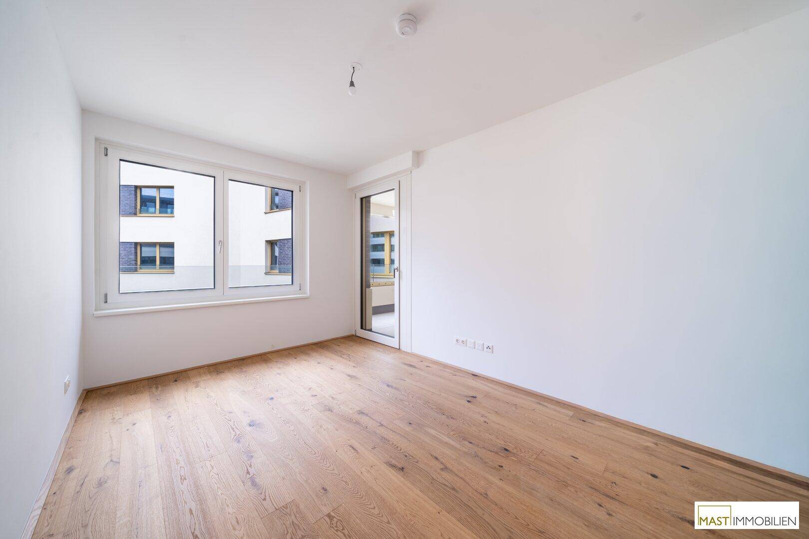 Helles Zimmer mit Parkettboden und großem Fenster, ideal als Schlaf- oder Arbeitszimmer.