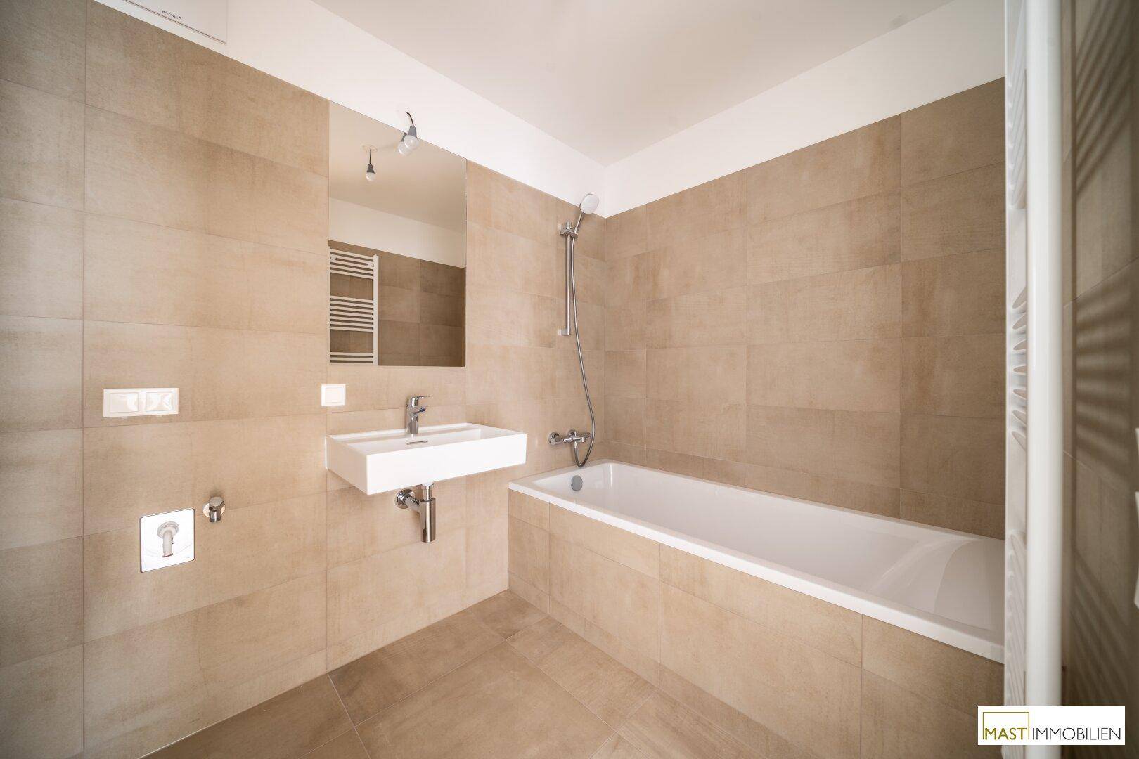 Modernes Badezimmer mit beigefarbenen Fliesen, einer Badewanne und einem einzelnen Waschbecken.