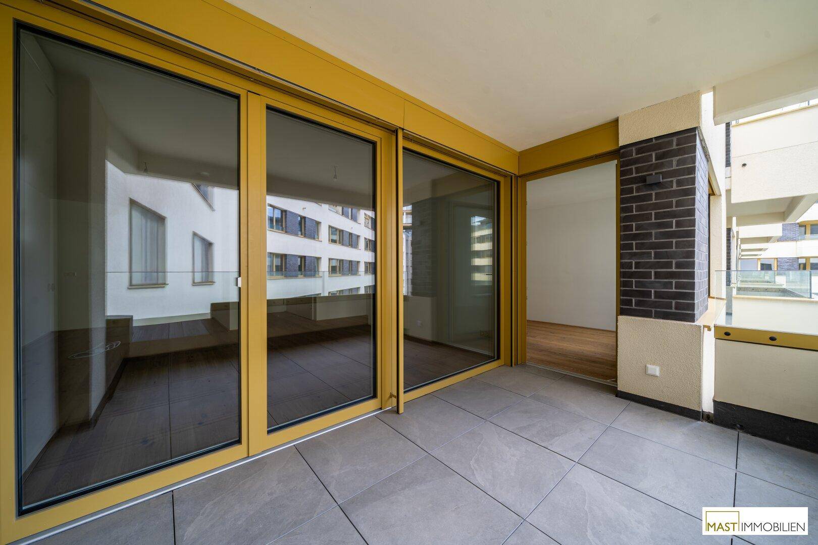 Geräumiger Balkon mit Fliesenboden und Blick auf die umliegenden Gebäude der Wohnanlage.
