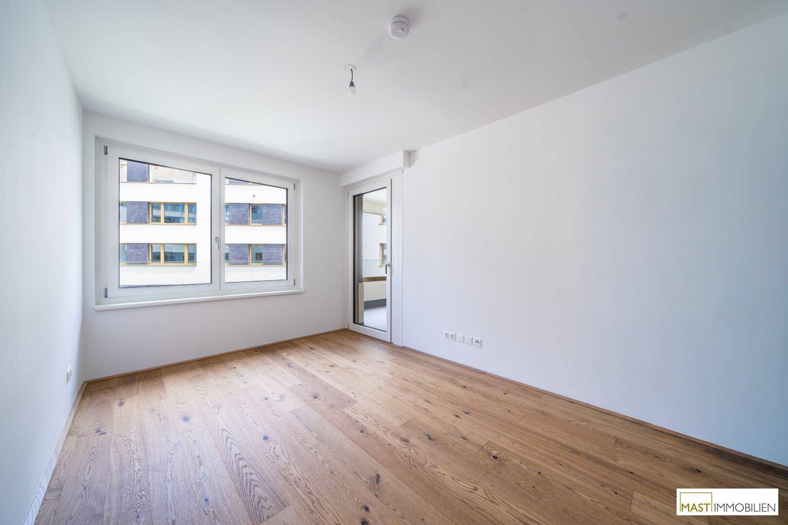 Helles Schlafzimmer mit Holzboden und einem Fenster, das viel Tageslicht hereinlässt.