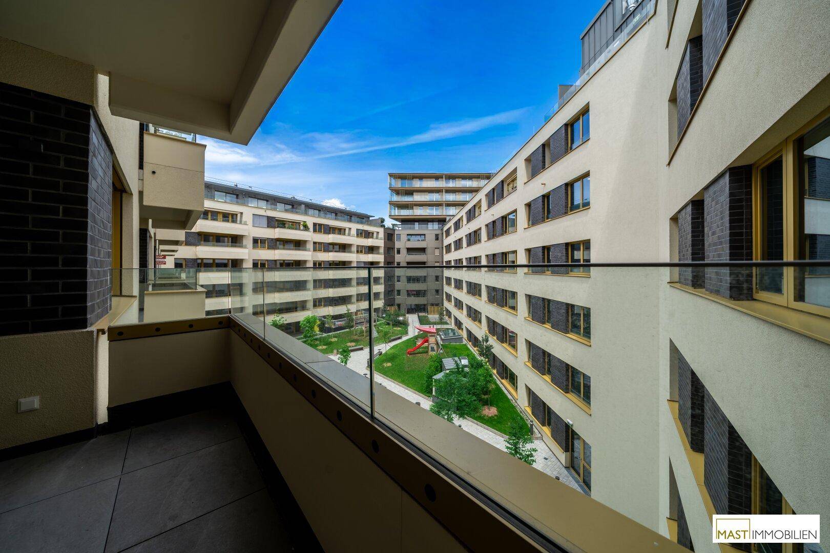 Balkon mit Glasbrüstung bietet einen schönen Blick auf den grünen Innenhof und den Kinderspielplatz.
